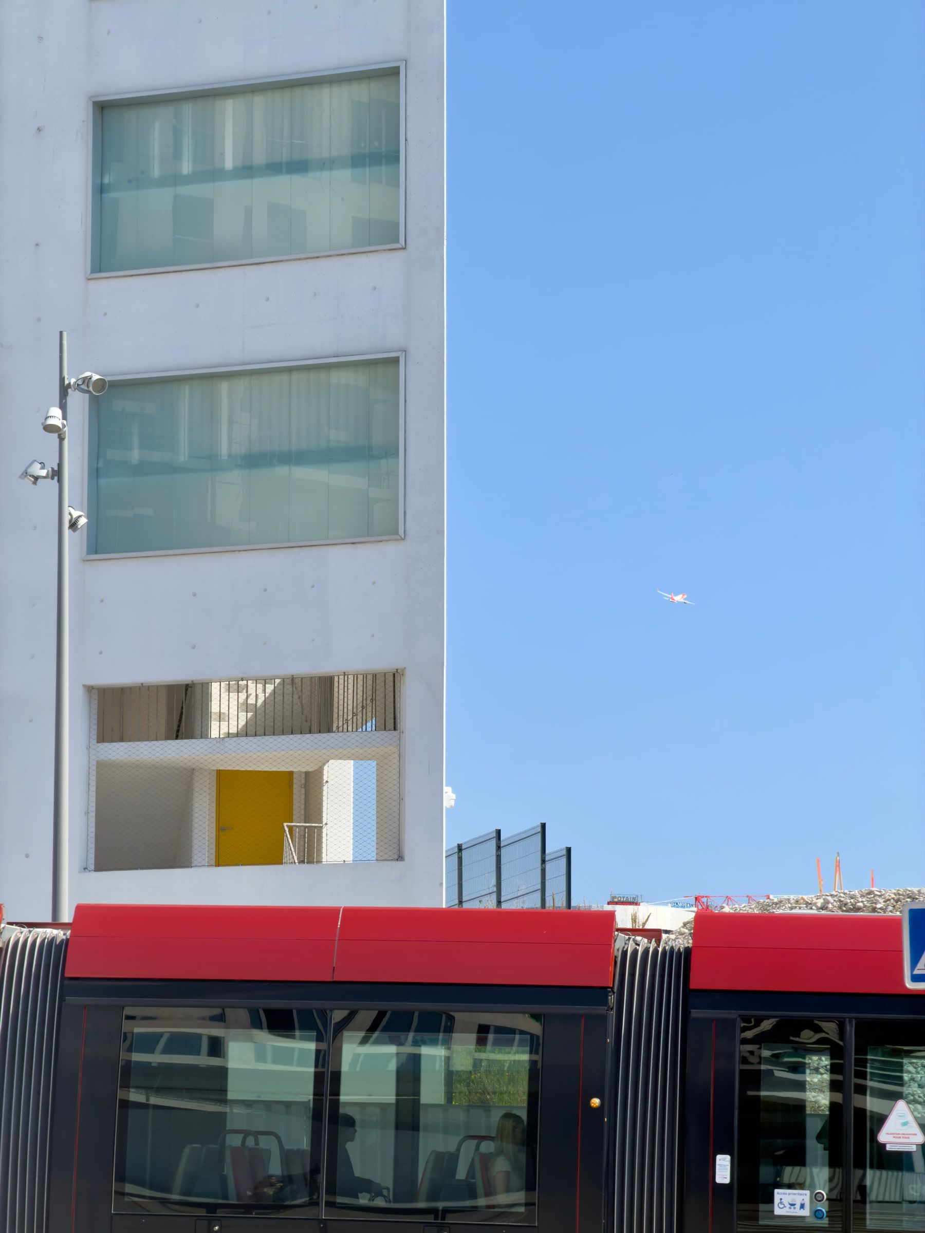 A red and black tram passing a white modern apartment building against a deep blue sky