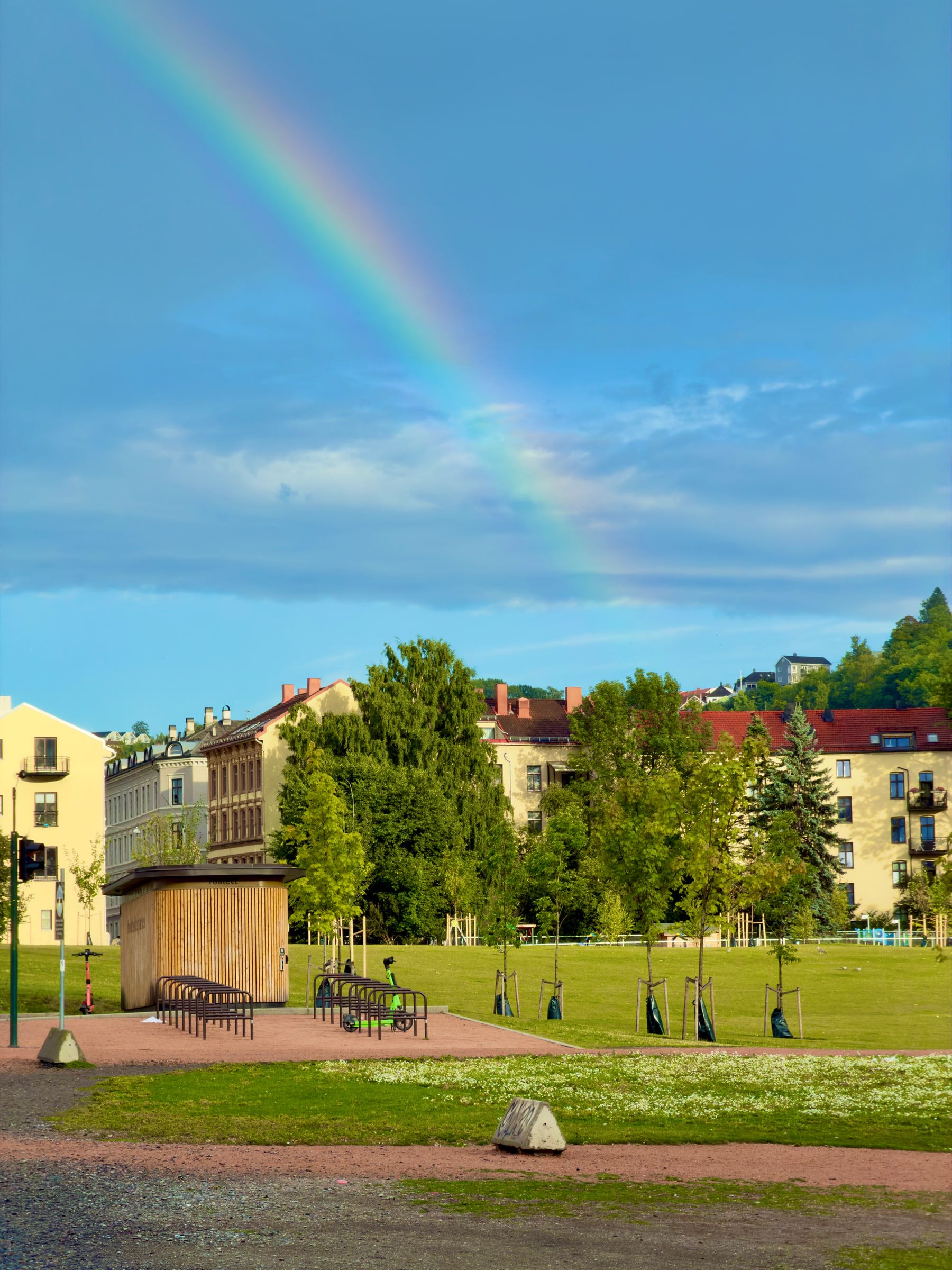 A rainbow arcing over a park of mown grass with pale apartment blocks and trees behind