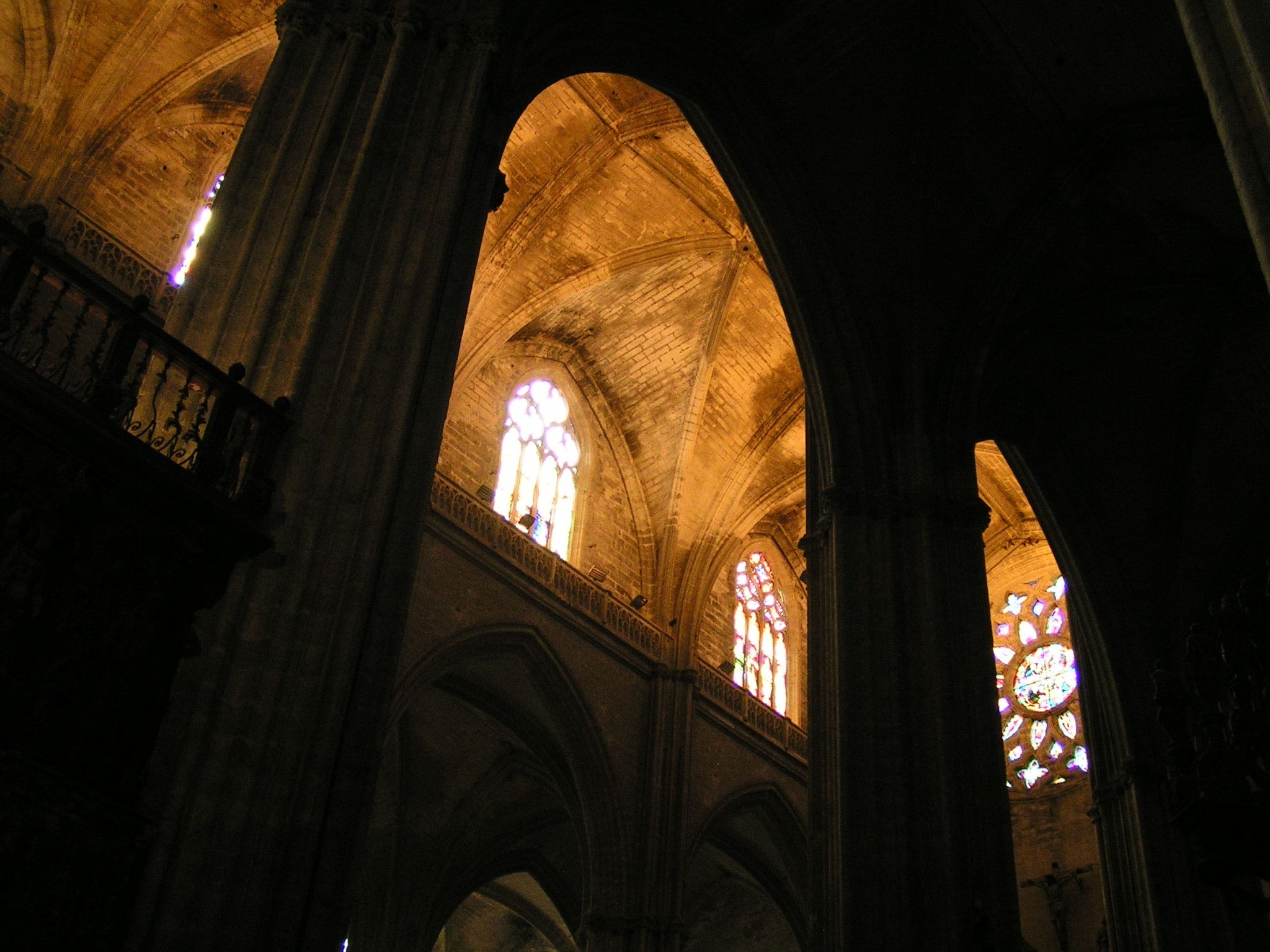The dark interior of a Gothic cathedral, massive columns and pointed arches receding toward lit stained-glass windows