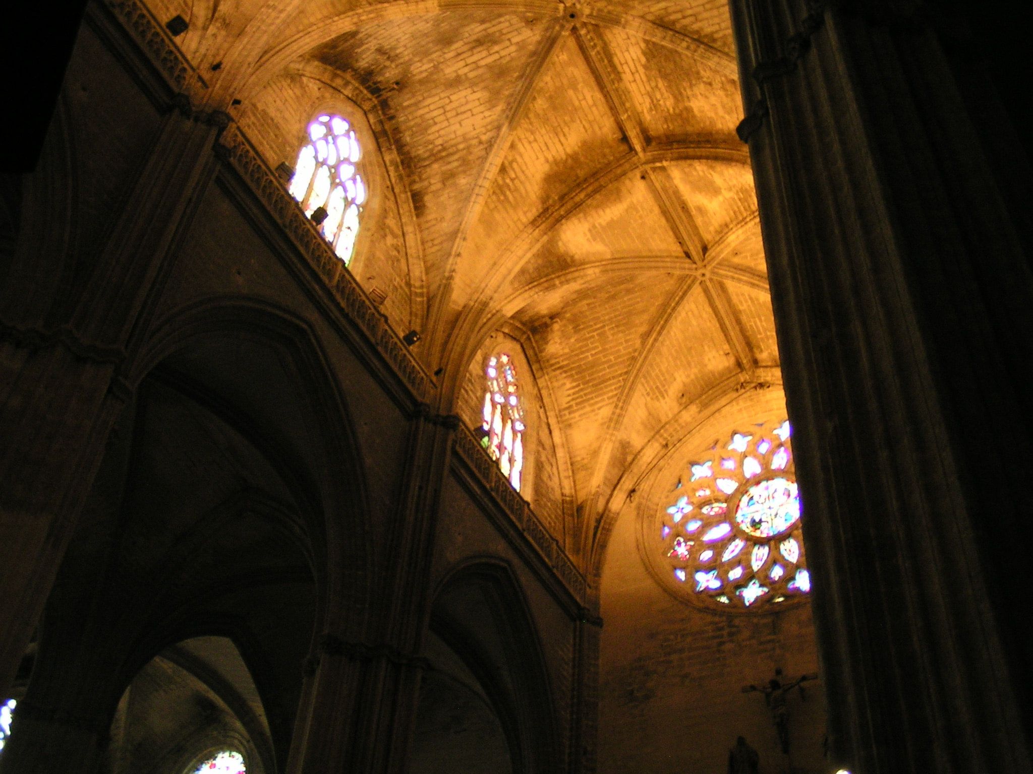Gothic stone vaults lit warm from below, with a rose window and tall lancet windows glowing violet in the wall beneath