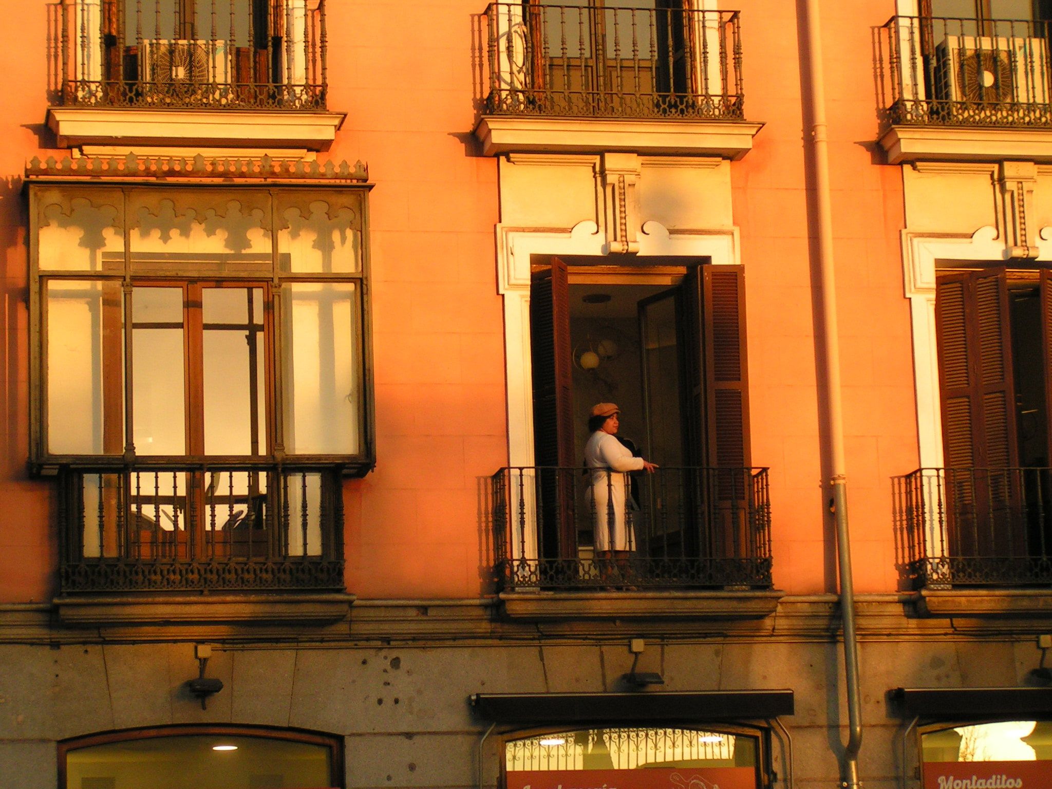 A warm ochre building facade lit gold by low evening sun, a person standing out on one of the wrought-iron balconies