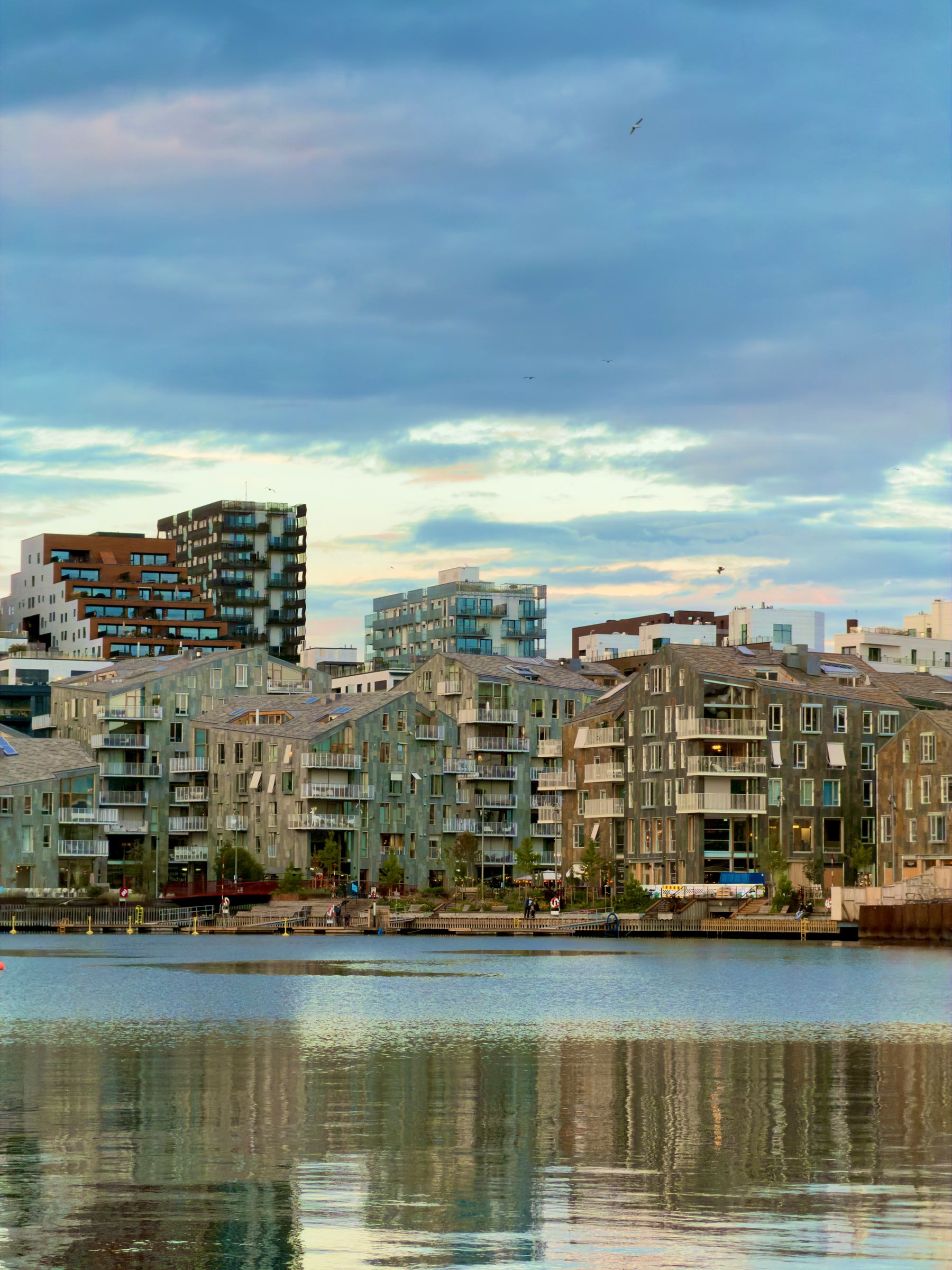 Waterfront apartment buildings across flat calm water under a pale evening sky
