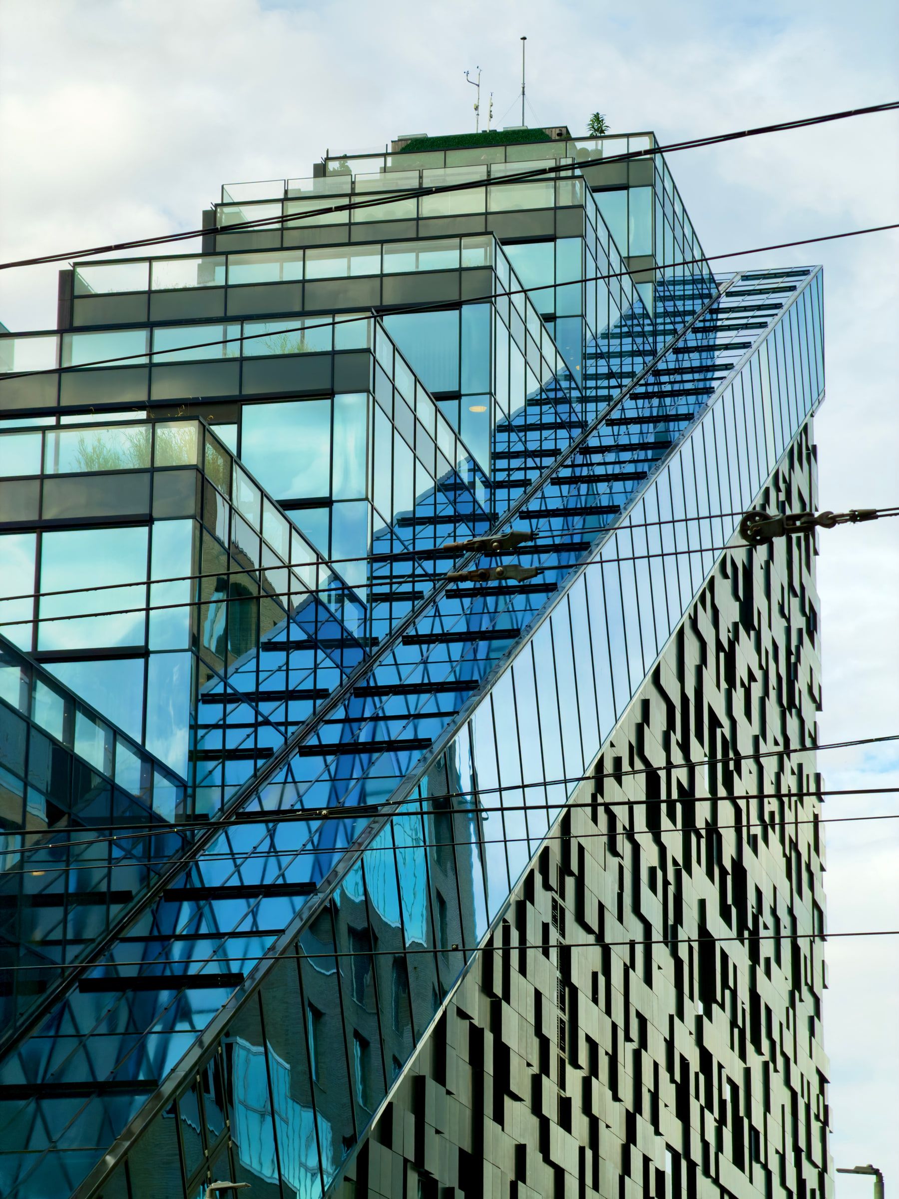 A glass office tower photographed from below, its facade folding into diagonal reflections of sky and cloud