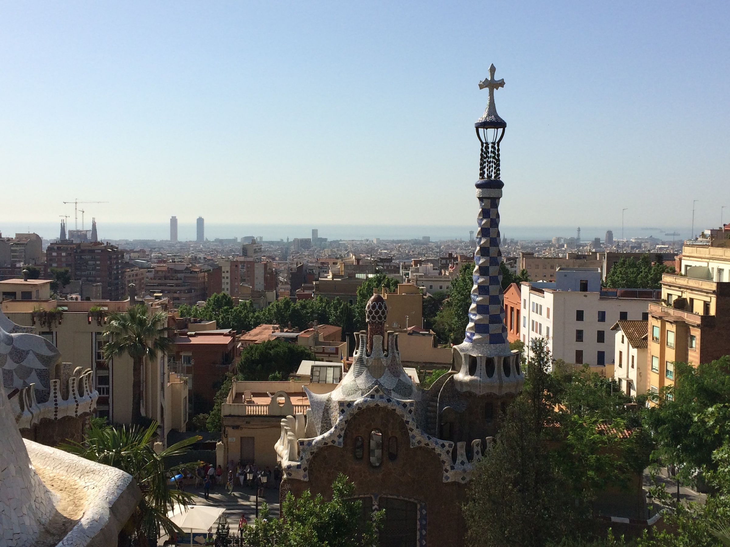 A view across a city to the sea from a terraced park, a tiled pavilion roof in the foreground