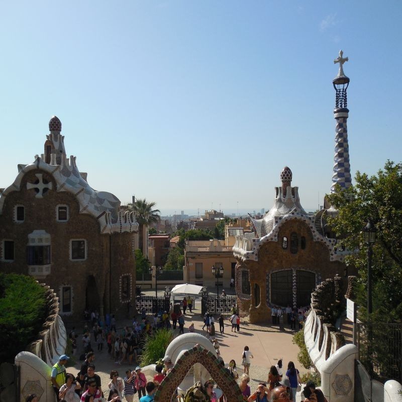 Two stone pavilions with undulating tiled roofs and a spired tower flanking a park entrance, visitors on the steps