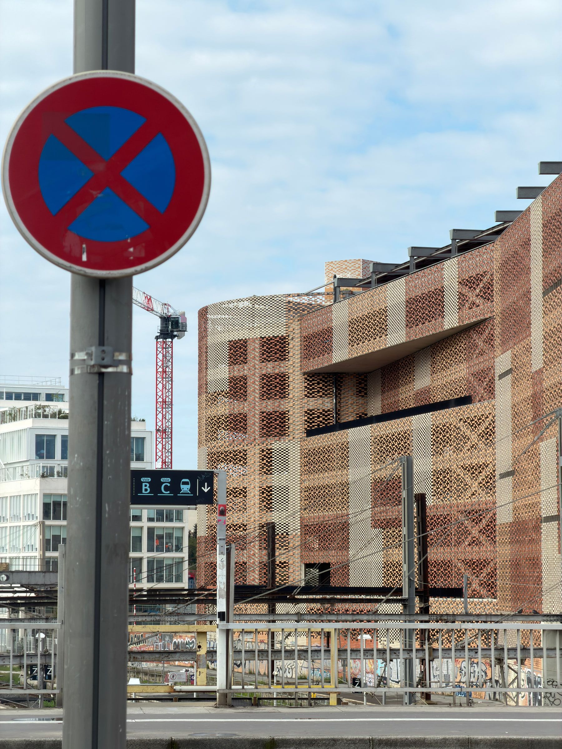 A no-stopping sign in the foreground with a large modern building of patterned brick and a construction crane behind