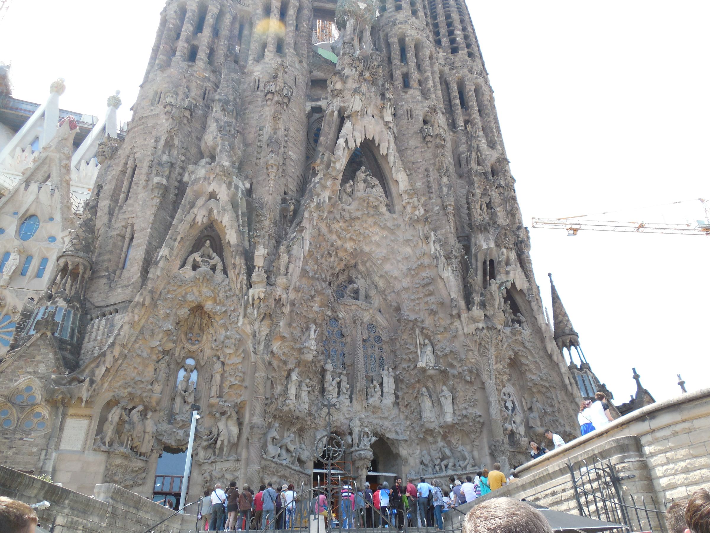 The densely carved Nativity facade of a large basilica, a queue of visitors at its doors