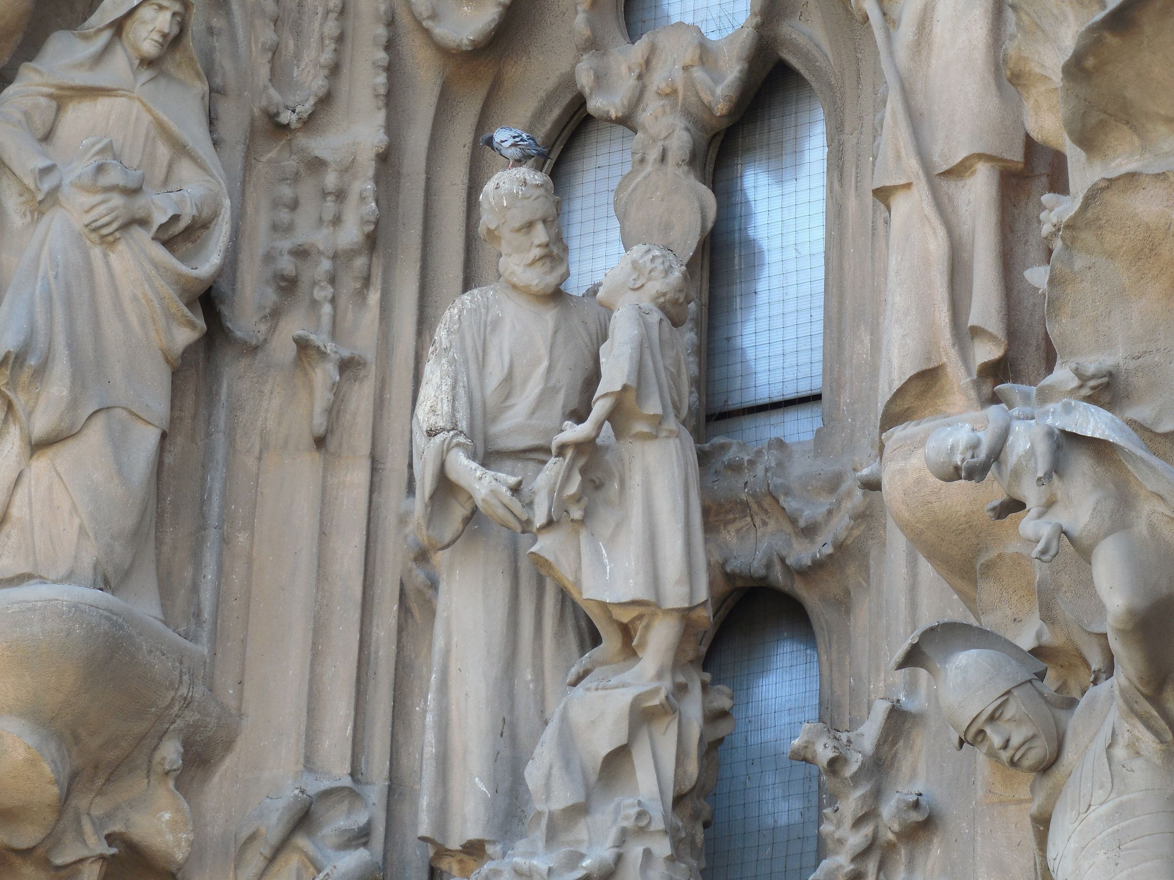 Angular stone figures on a church facade, cut flat and hard against plain gridded windows