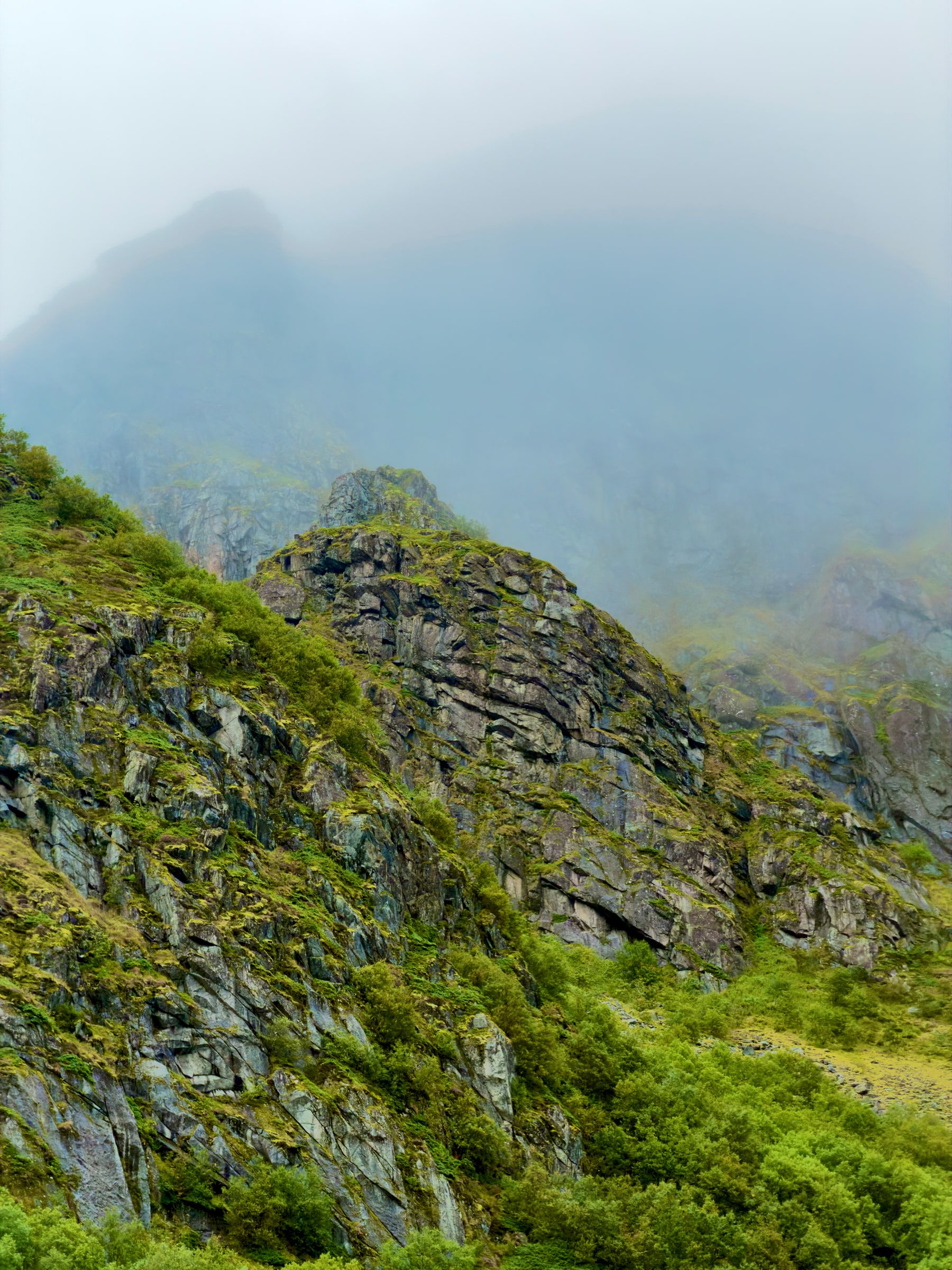 A green and grey mountain ridge with cloud sitting on the rock above it