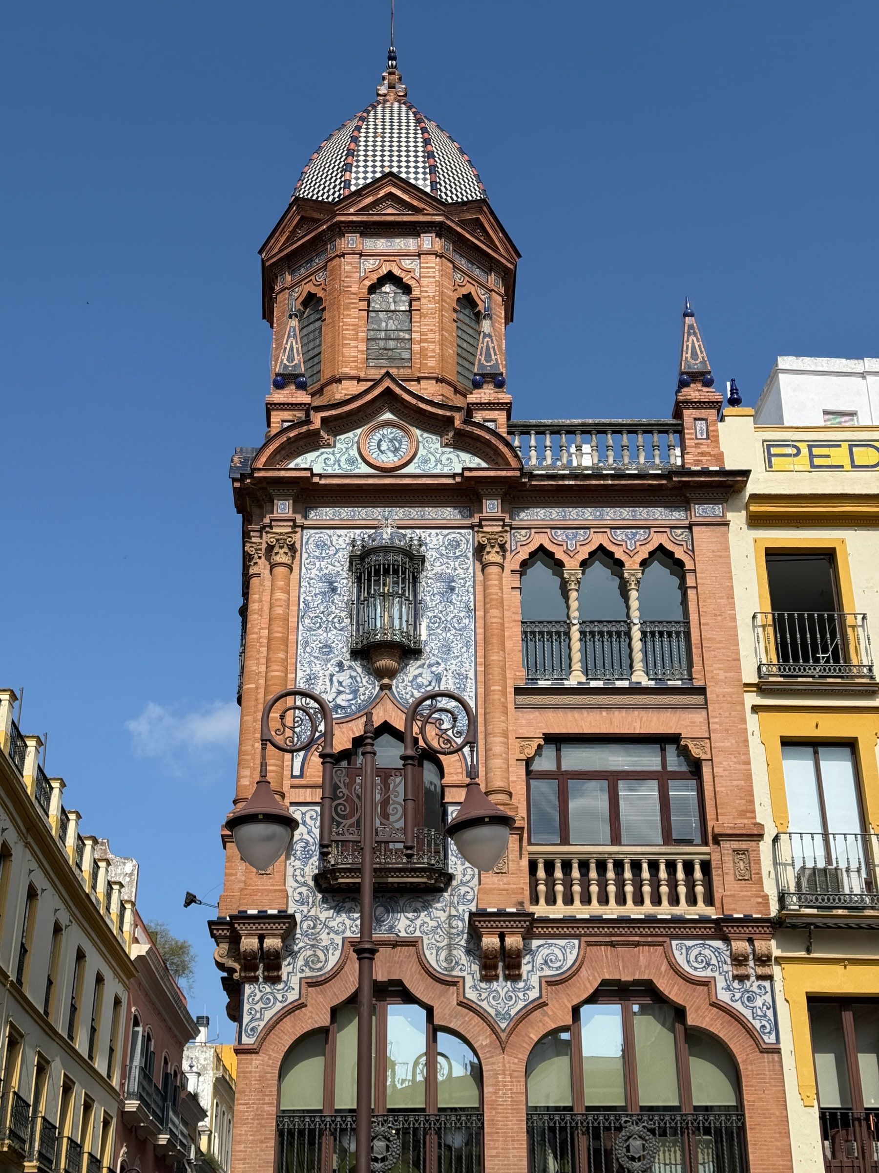 An ornate brick corner building set with blue-and-white tiled panels, a glazed balcony and a tiled turret dome, against a deep blue sky