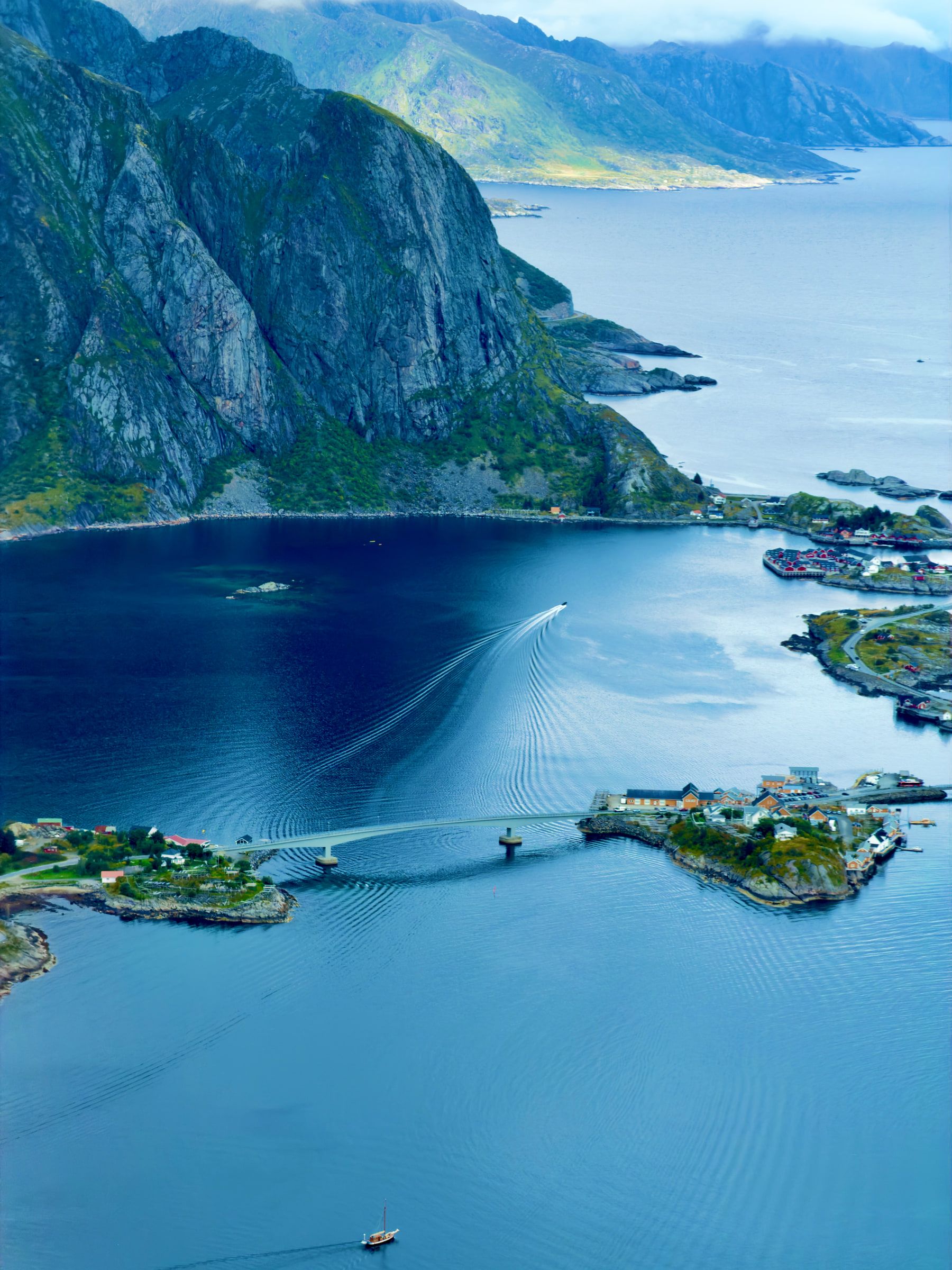 A low bridge linking rocky islets across deep blue water, a boat drawing a white wake beneath it