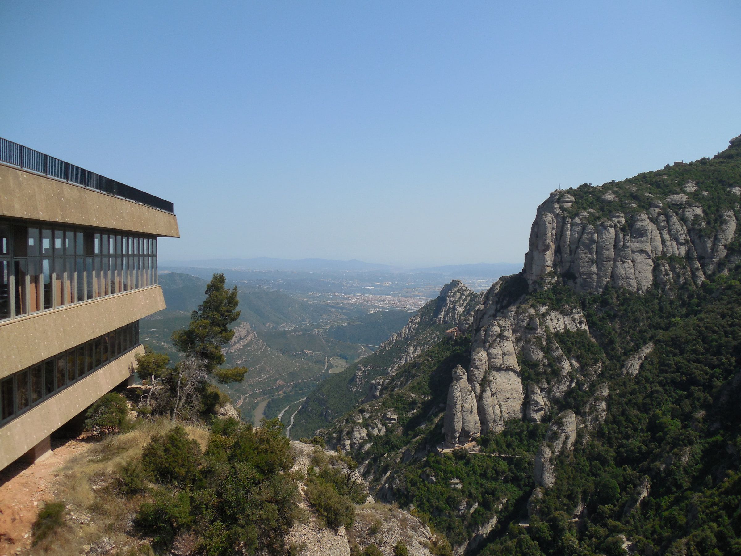 A modern building standing at a cliff edge above a deep valley, rock pinnacles rising opposite