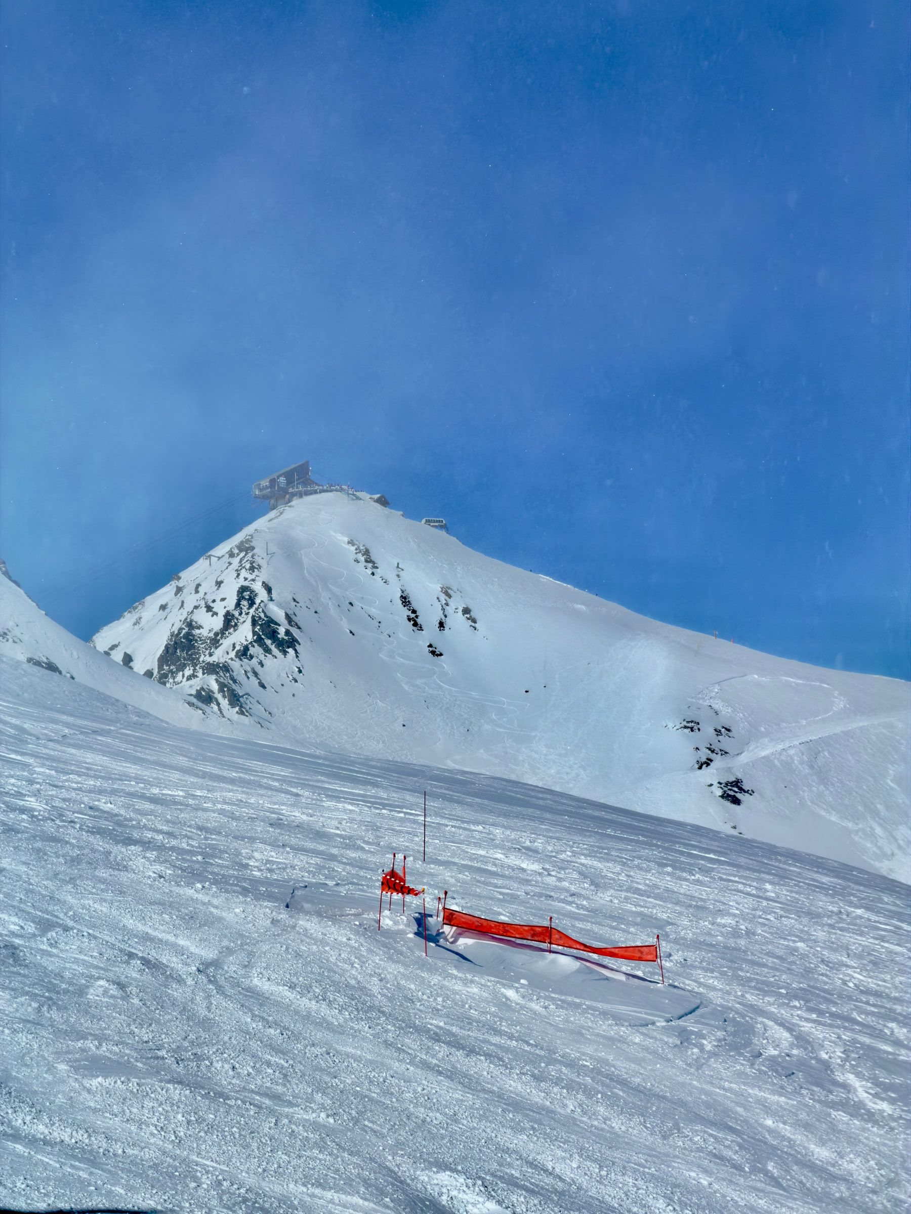 A snow ridge under deep blue sky with a line of orange safety netting staked across it