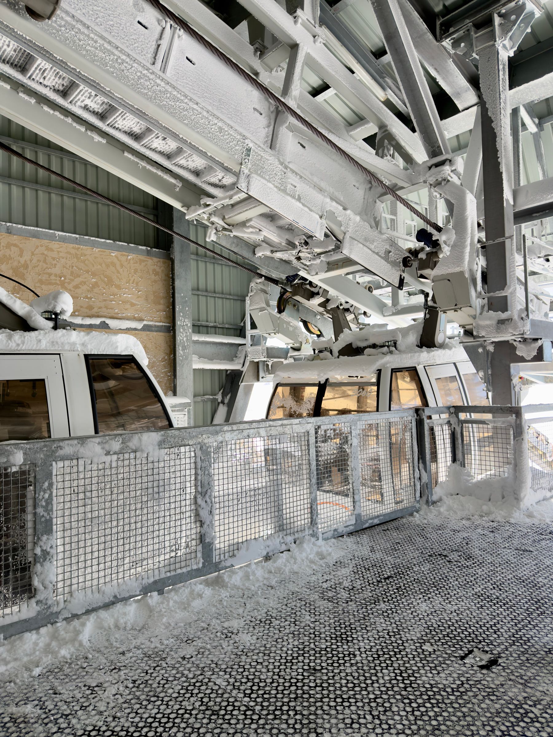 The inside of a gondola station, empty cabins parked in a line under steel trusses above a metal grating floor