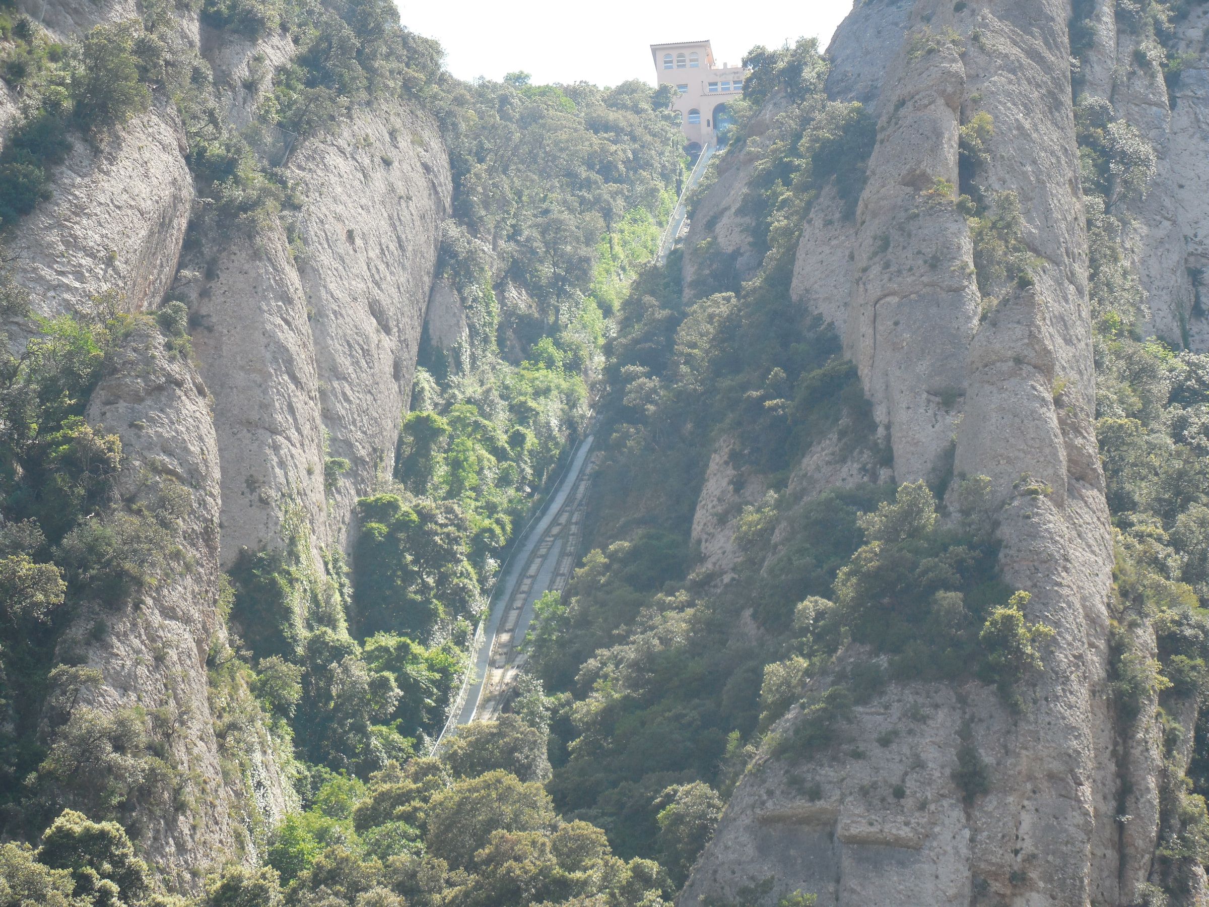 A funicular line running straight up a steep rock face between trees, a station at the top