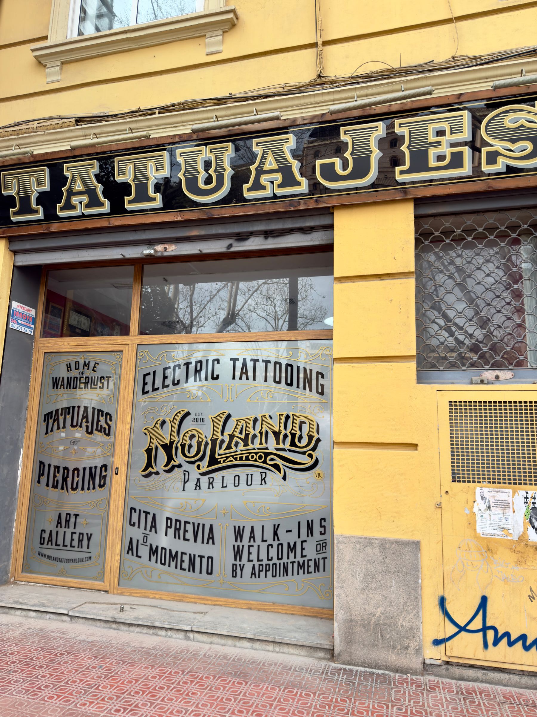 A yellow-fronted tattoo parlour with hand-painted gold lettering reading Tatuajes across its windows