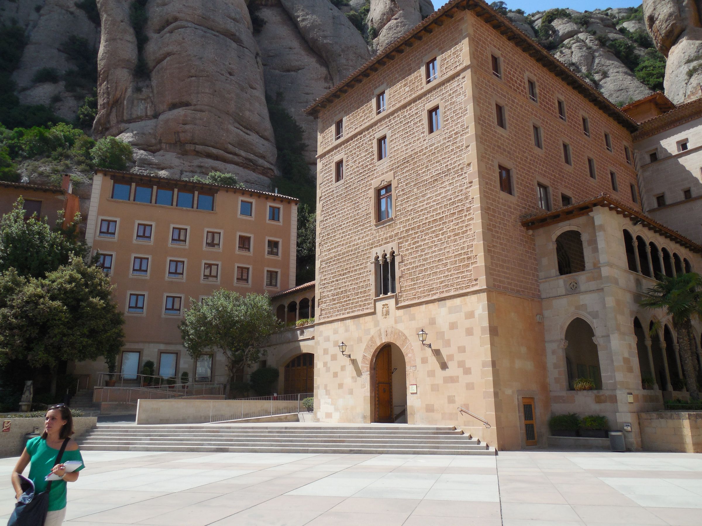 A monastery courtyard of tall ochre and stone buildings with rock formations rising directly behind