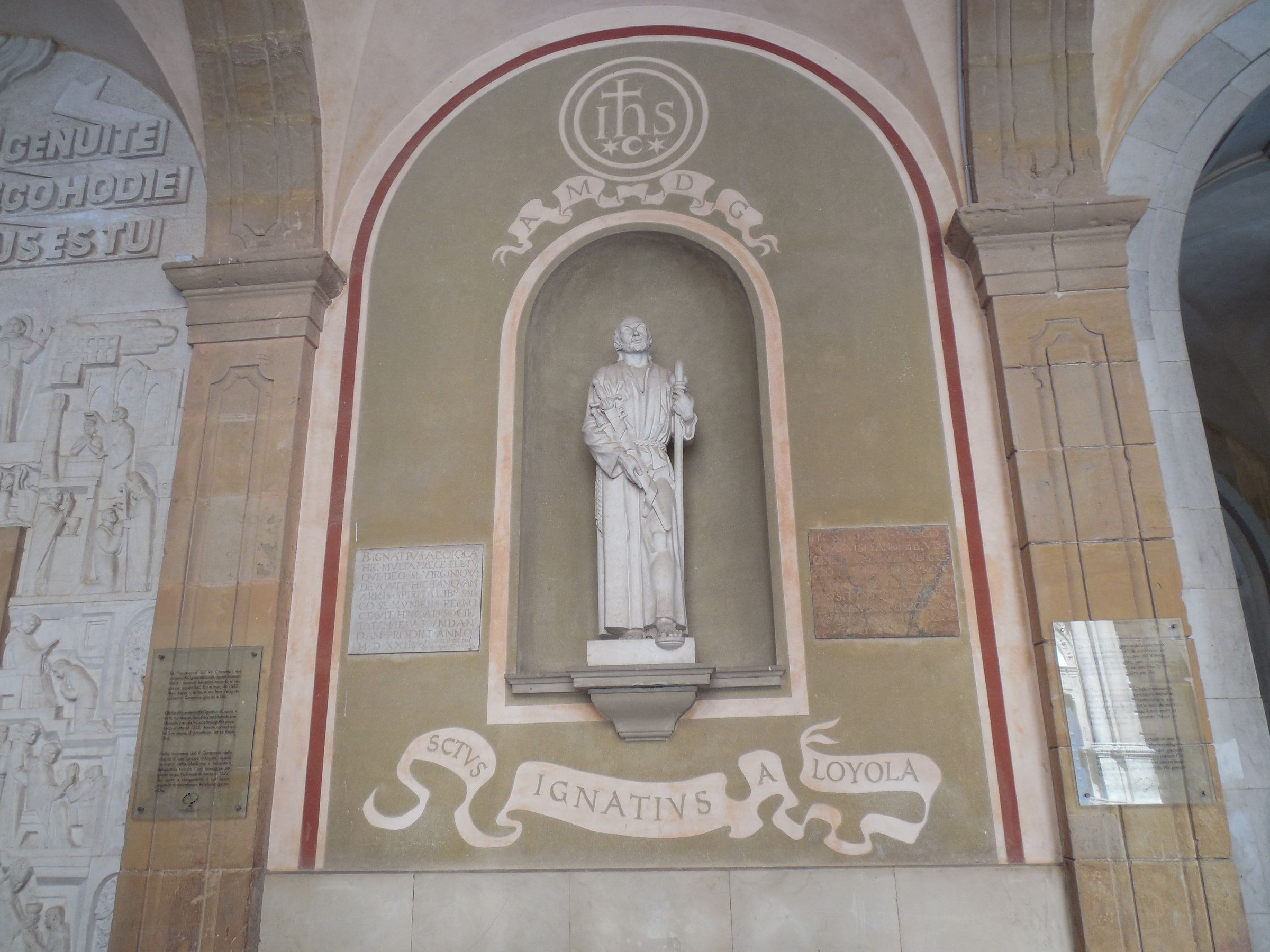 A painted wall niche holding a pale statue, a scrolled banner reading Sanctus Ignatius a Loyola beneath it