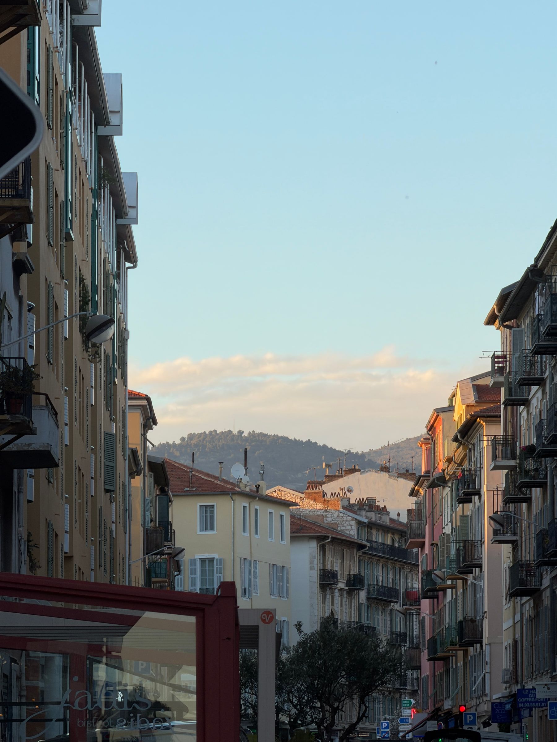 A street of ochre and pink buildings with shutters and balconies, hills closing off the far end in evening light