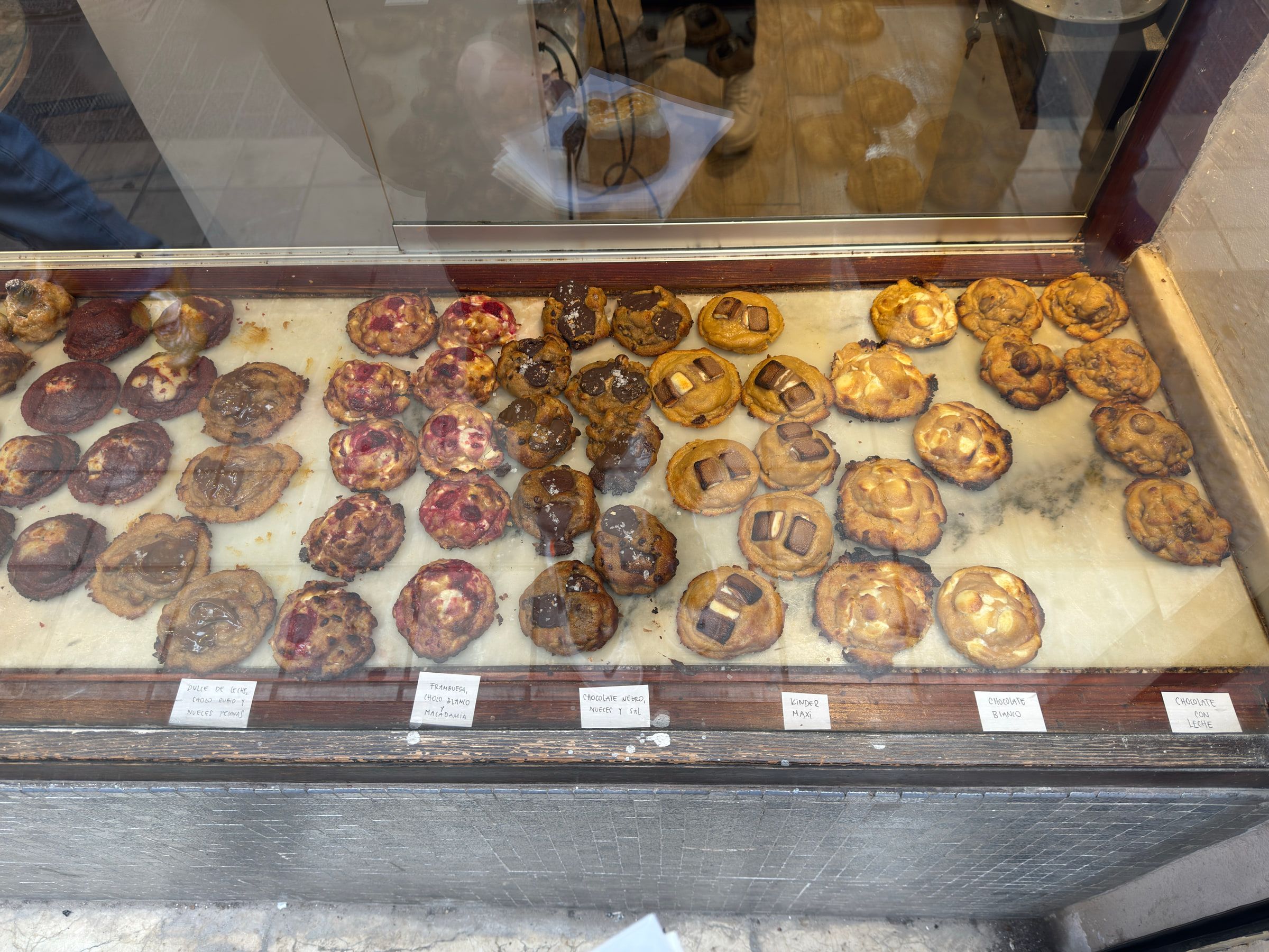 A bakery window display of filled and glazed pastries laid out in rows, each group named on a small handwritten card