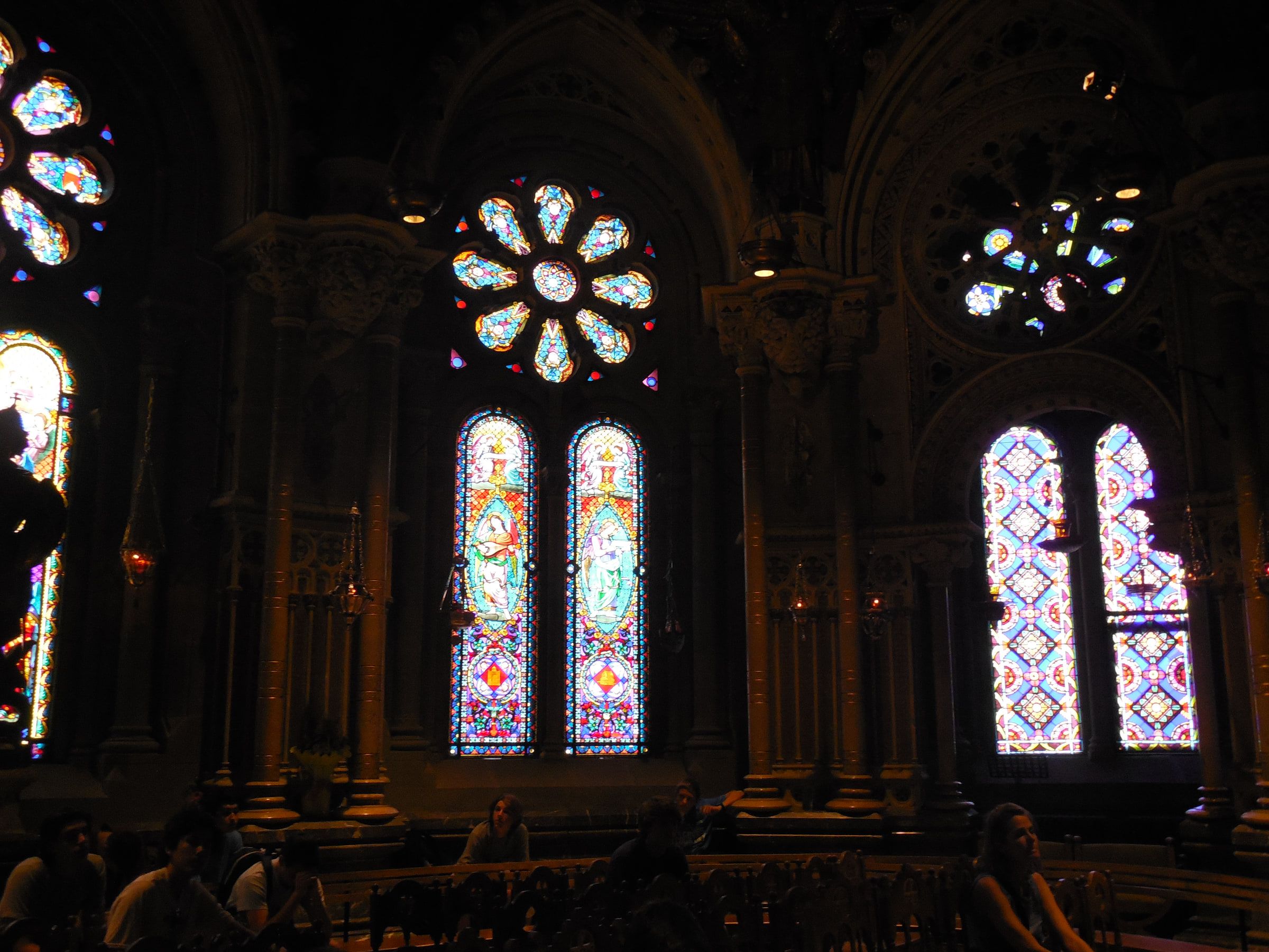 The dark interior of a basilica, a rose window and tall stained-glass lancets glowing along the wall