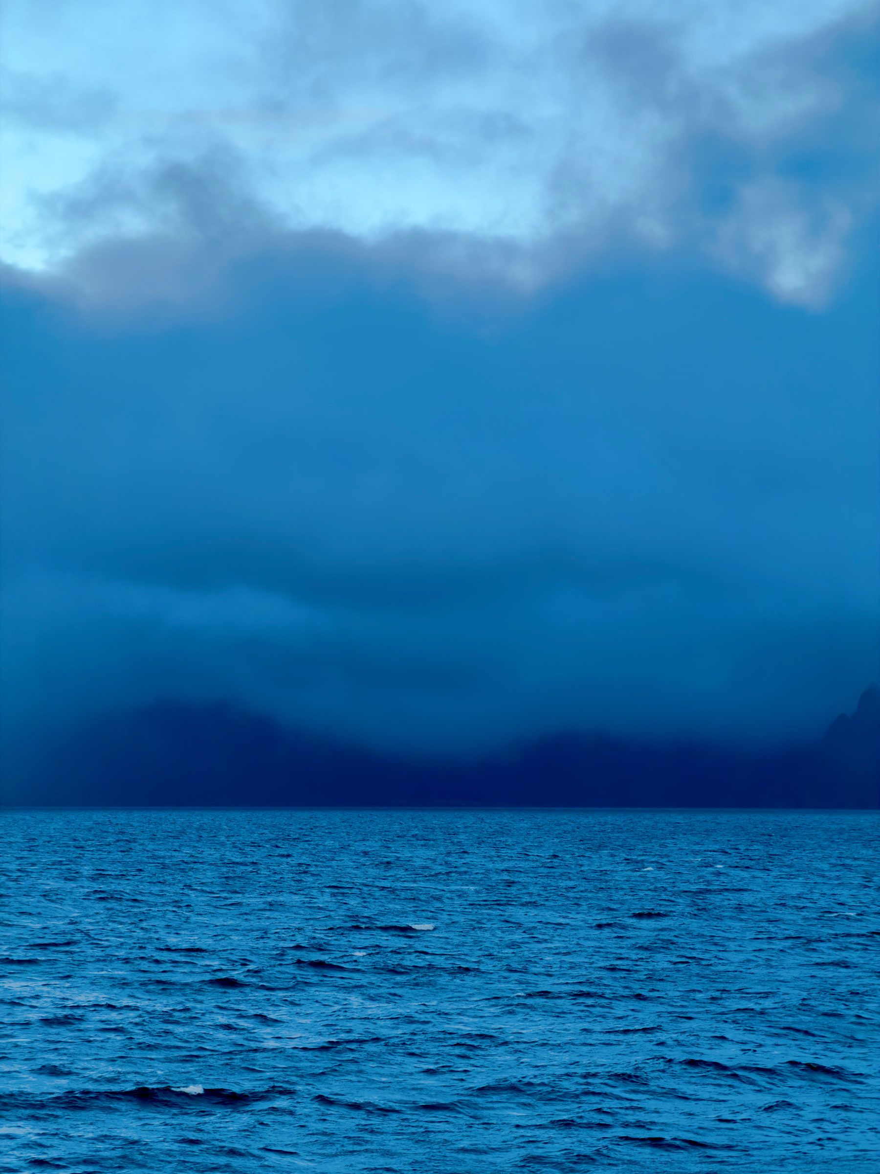 Low cloud sitting directly on dark open sea, a faint dark shore behind it