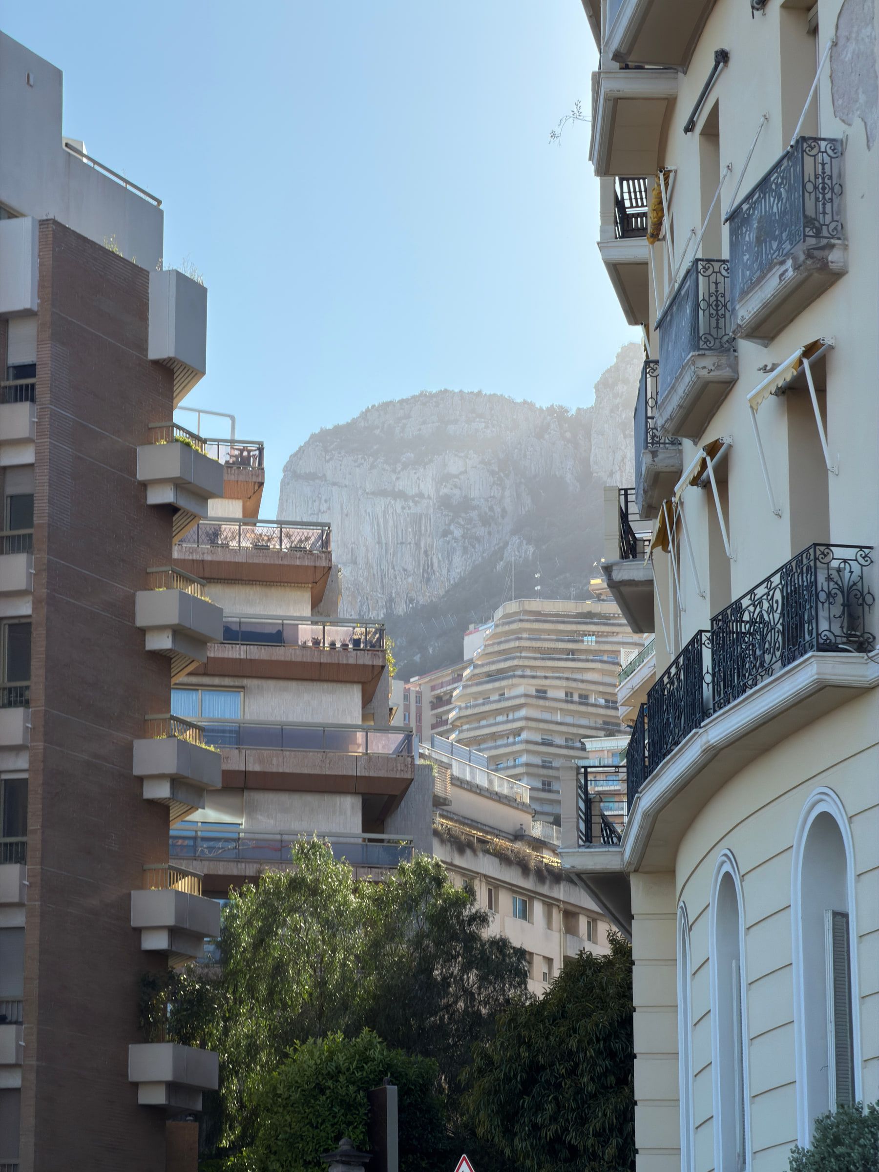 Modern terraced apartment blocks stacked against a pale limestone cliff, seen past an older balconied facade in the foreground