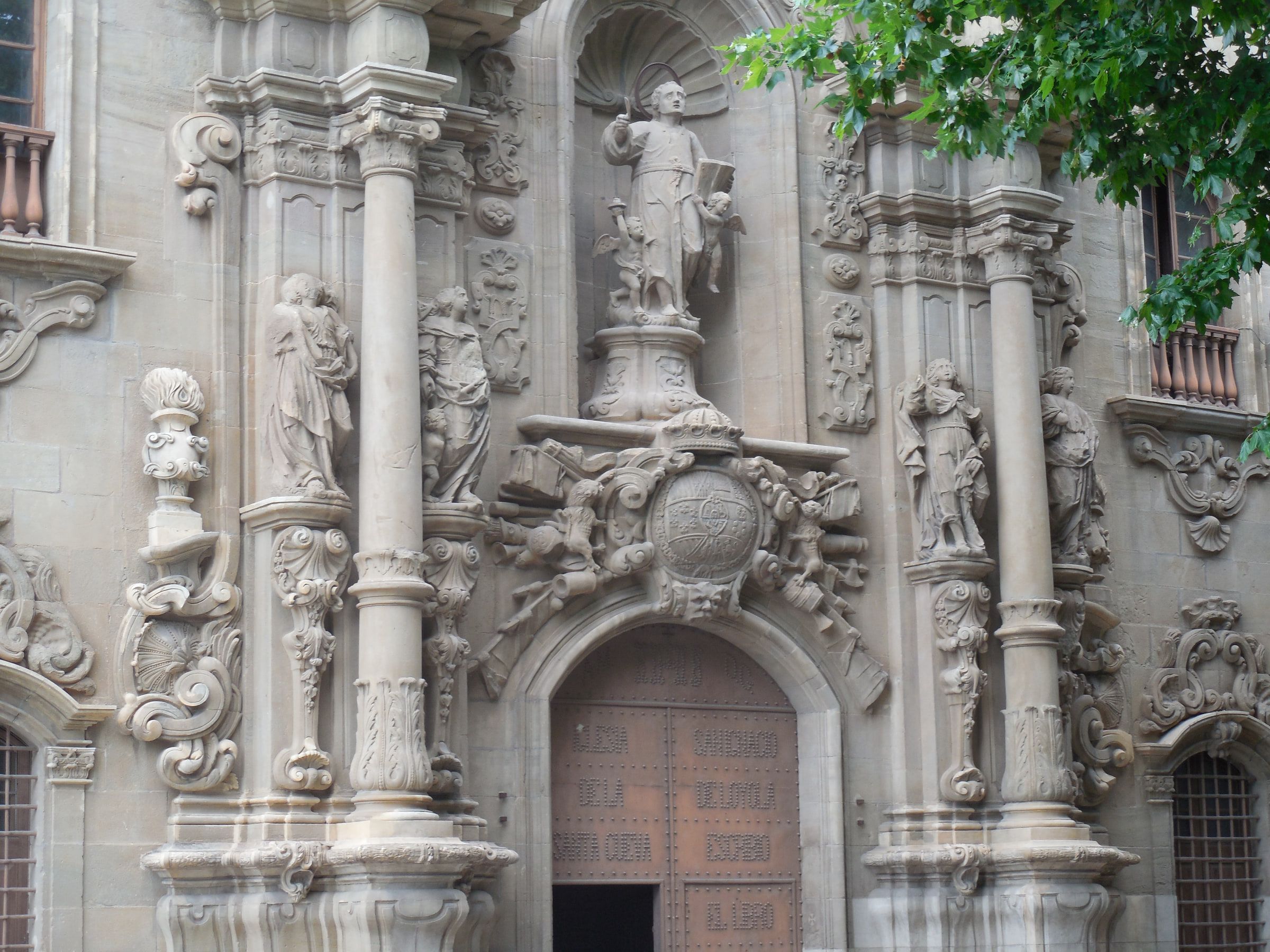 An elaborately carved baroque church facade with statues set between columns, framed by a tree