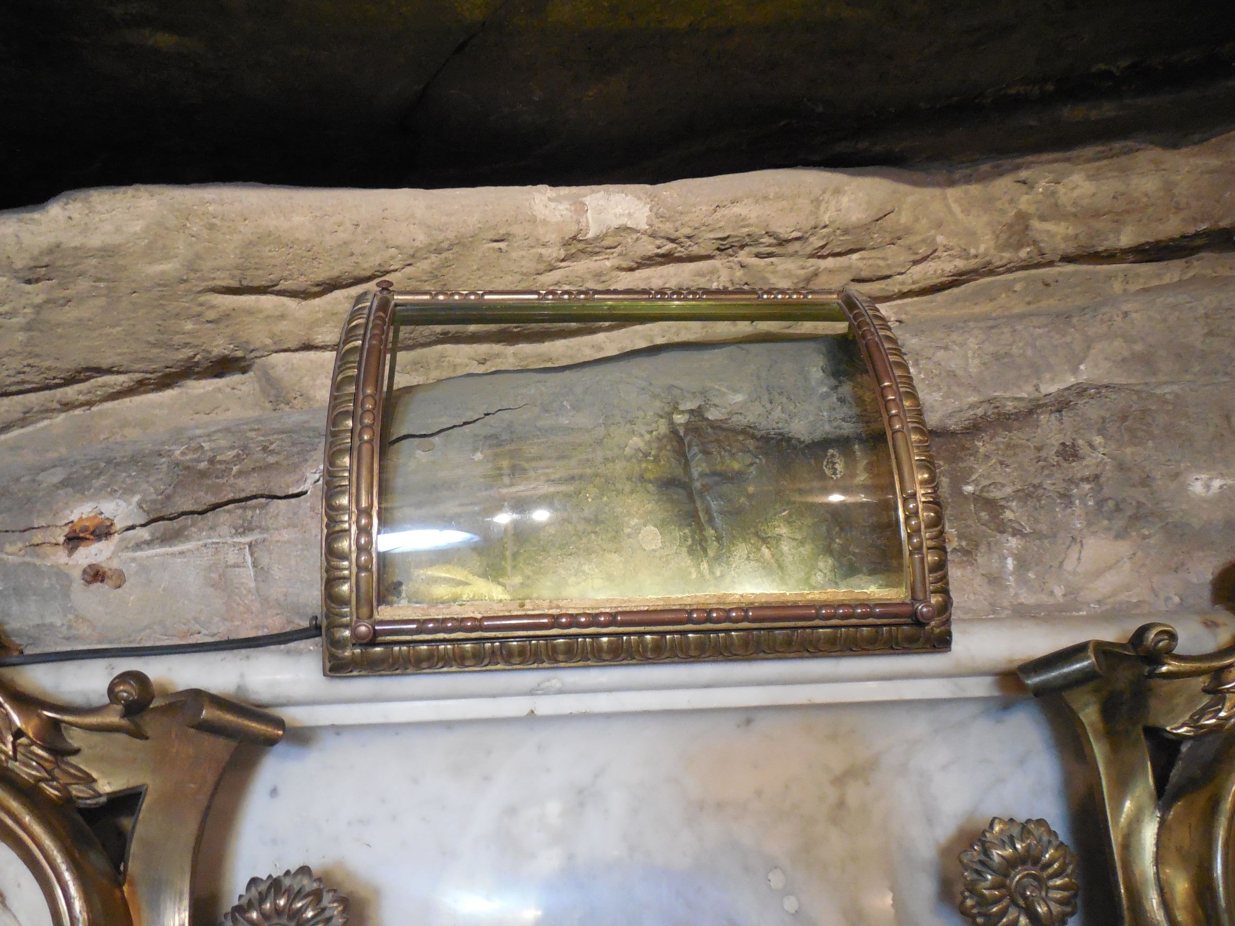 A gilded glass case set into bare rock inside a cave shrine, marble and giltwork below it