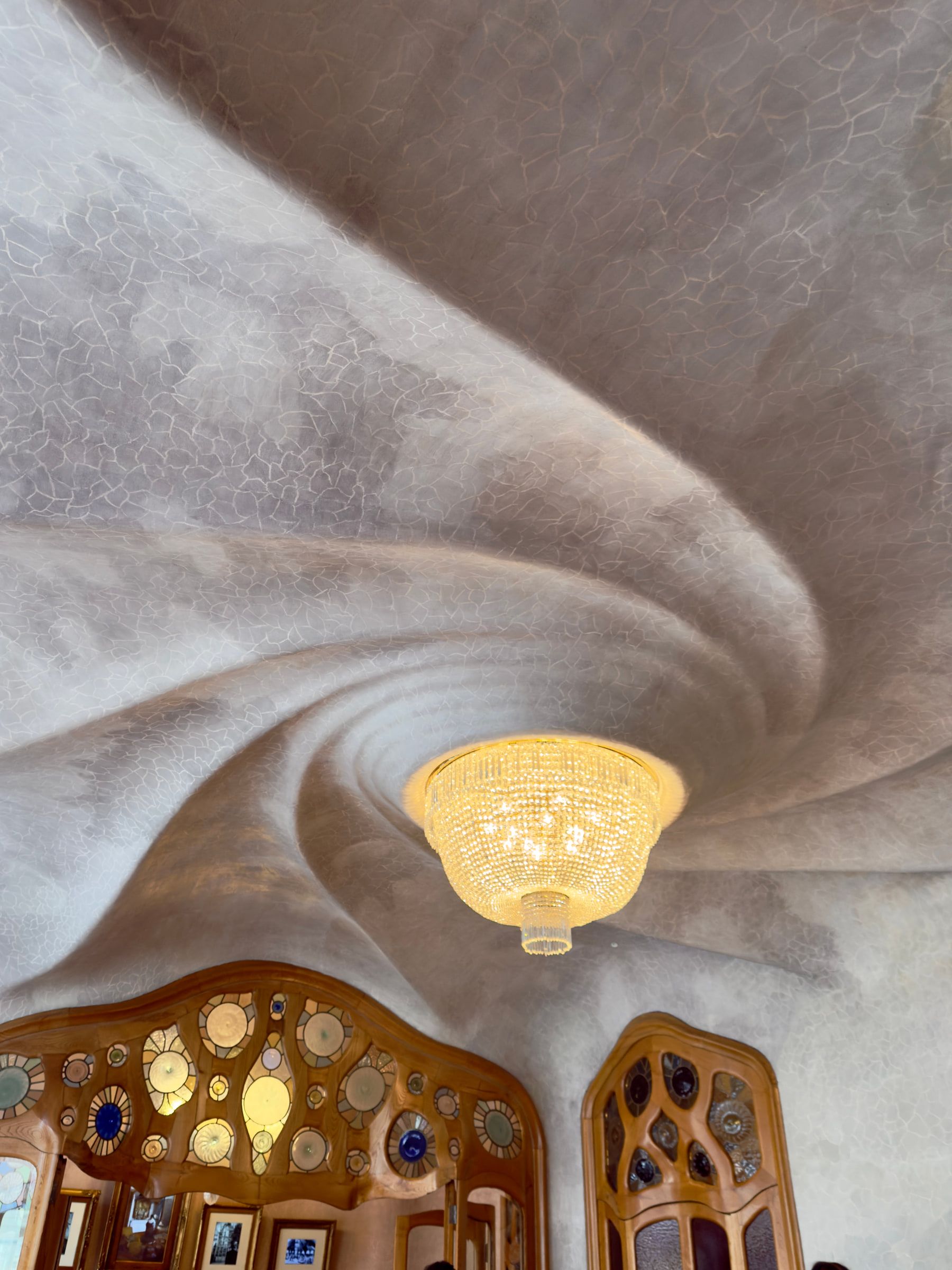 A white plaster ceiling swirling in a spiral around a crystal chandelier, ornate stained-glass doors below