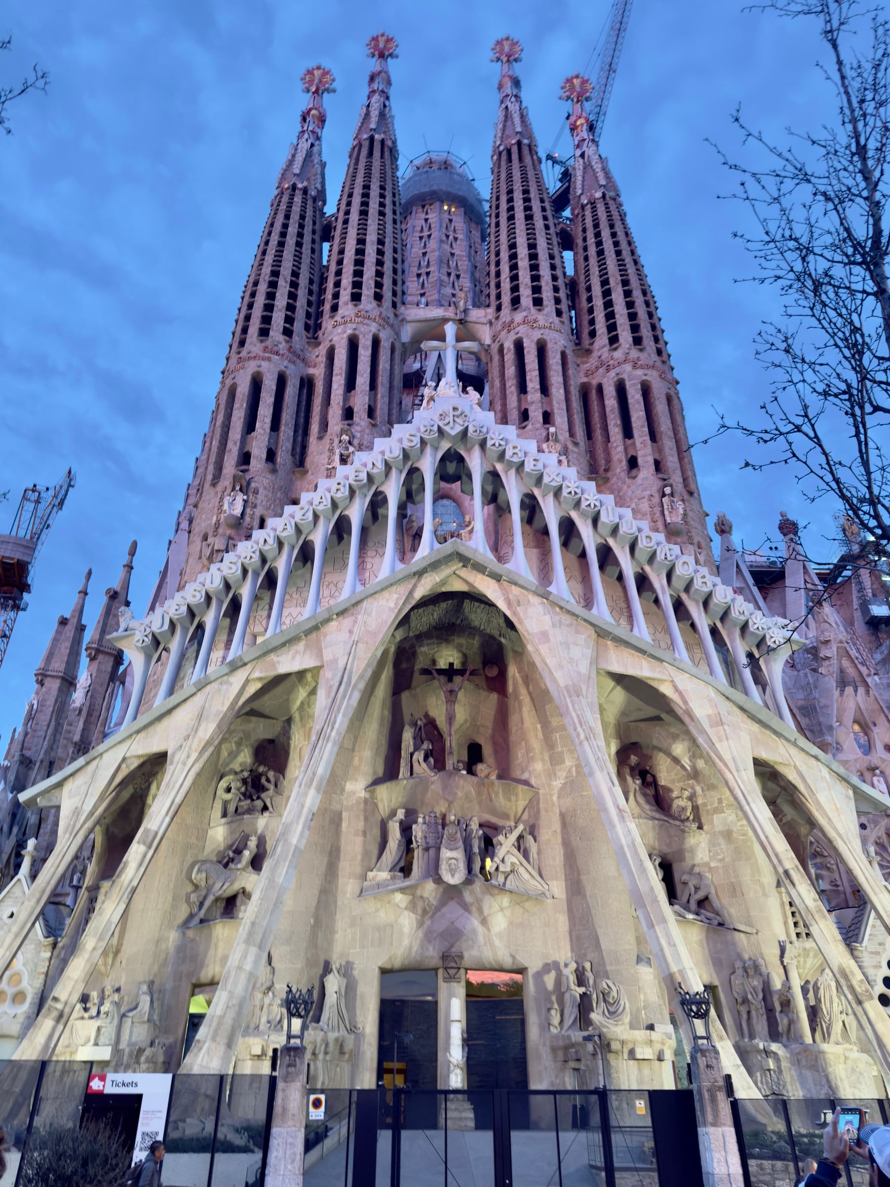 The ornate stone facade and spires of a large basilica photographed steeply from below against a deep blue evening sky