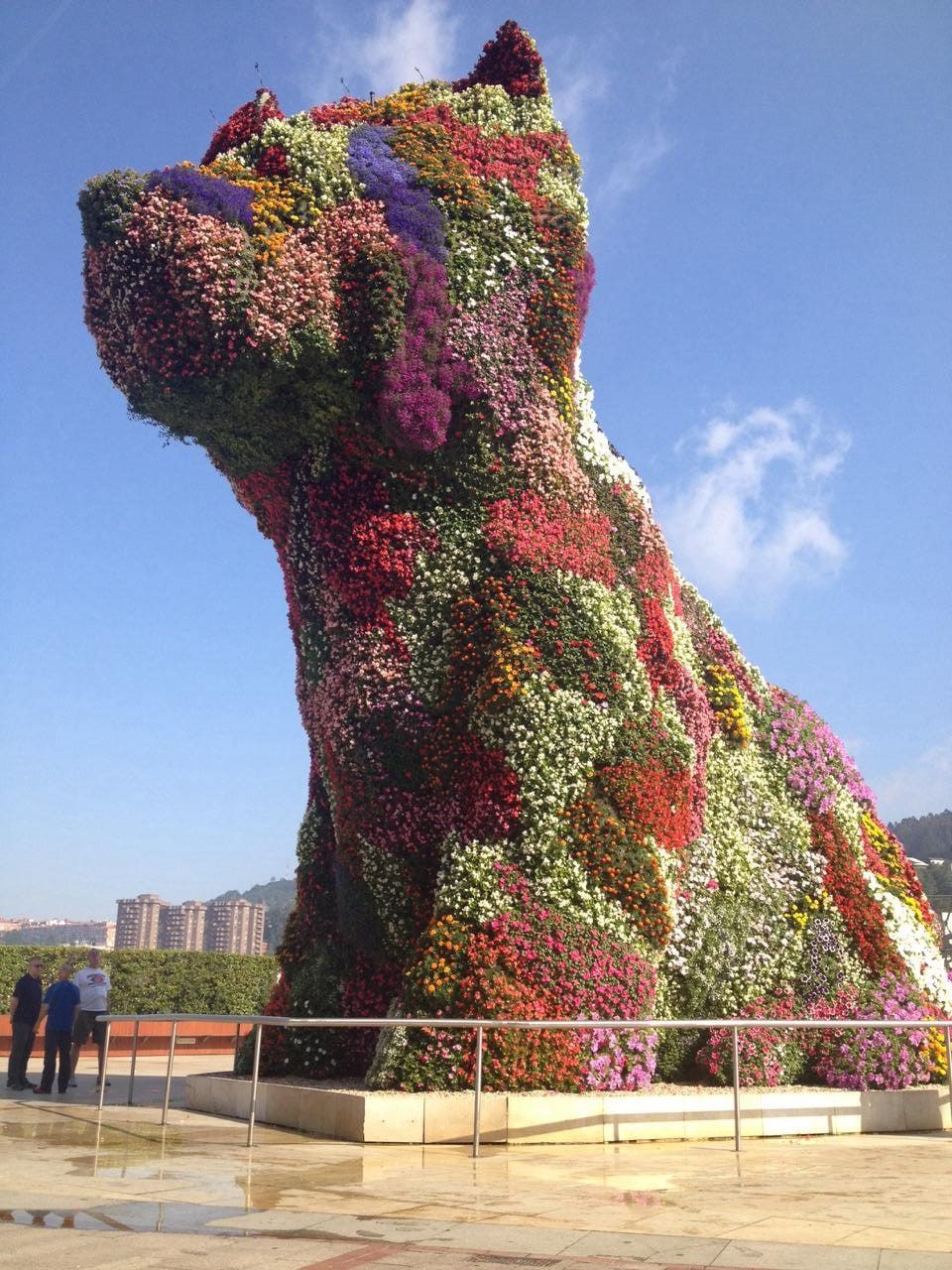 A vast sculpture of a seated dog covered entirely in flowering bedding plants, standing on a plaza