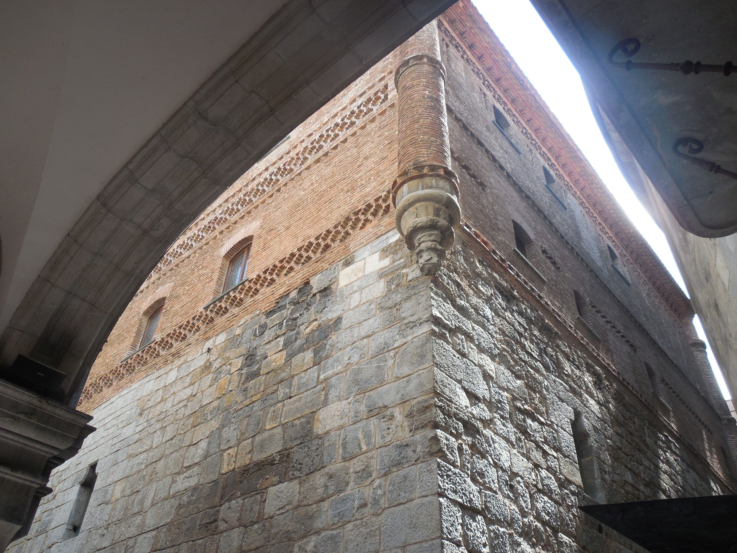 The corner of a fortified tower house, rough stone below and patterned brick above, seen sharply from beneath