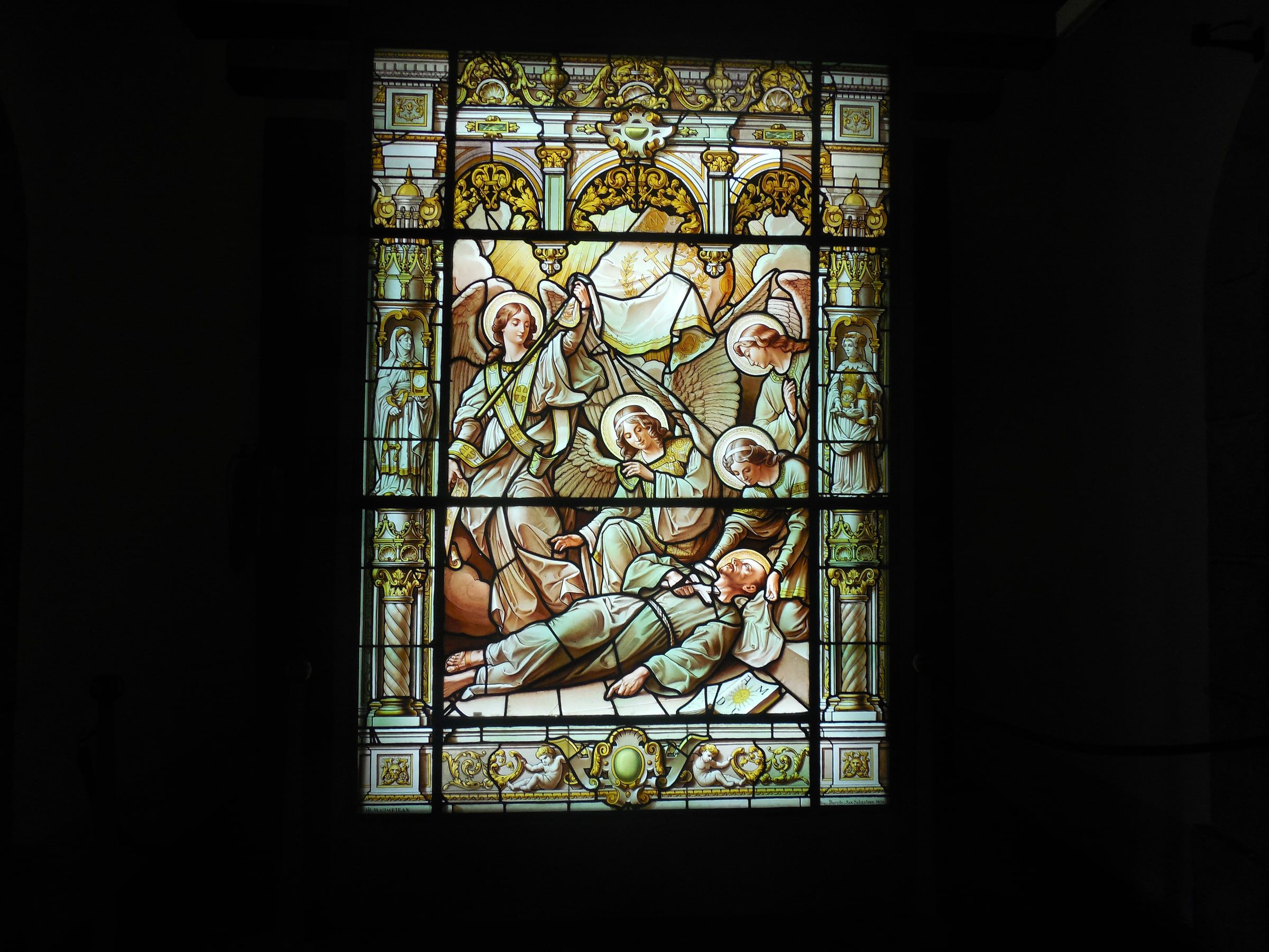 A stained-glass window showing a figure lying on a deathbed attended by others