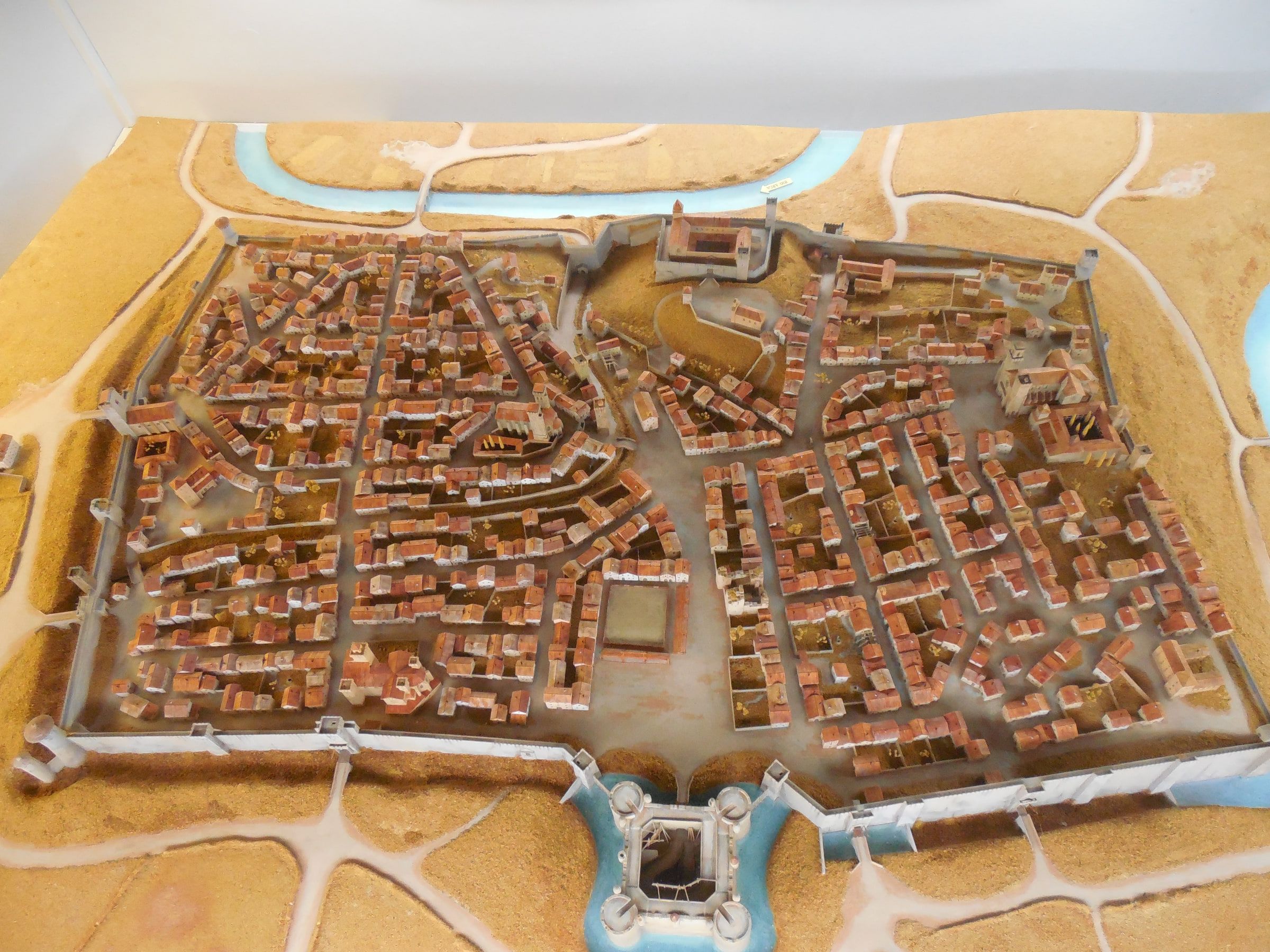 A tabletop relief model of a walled town with red roofs, its rivers marked in pale blue