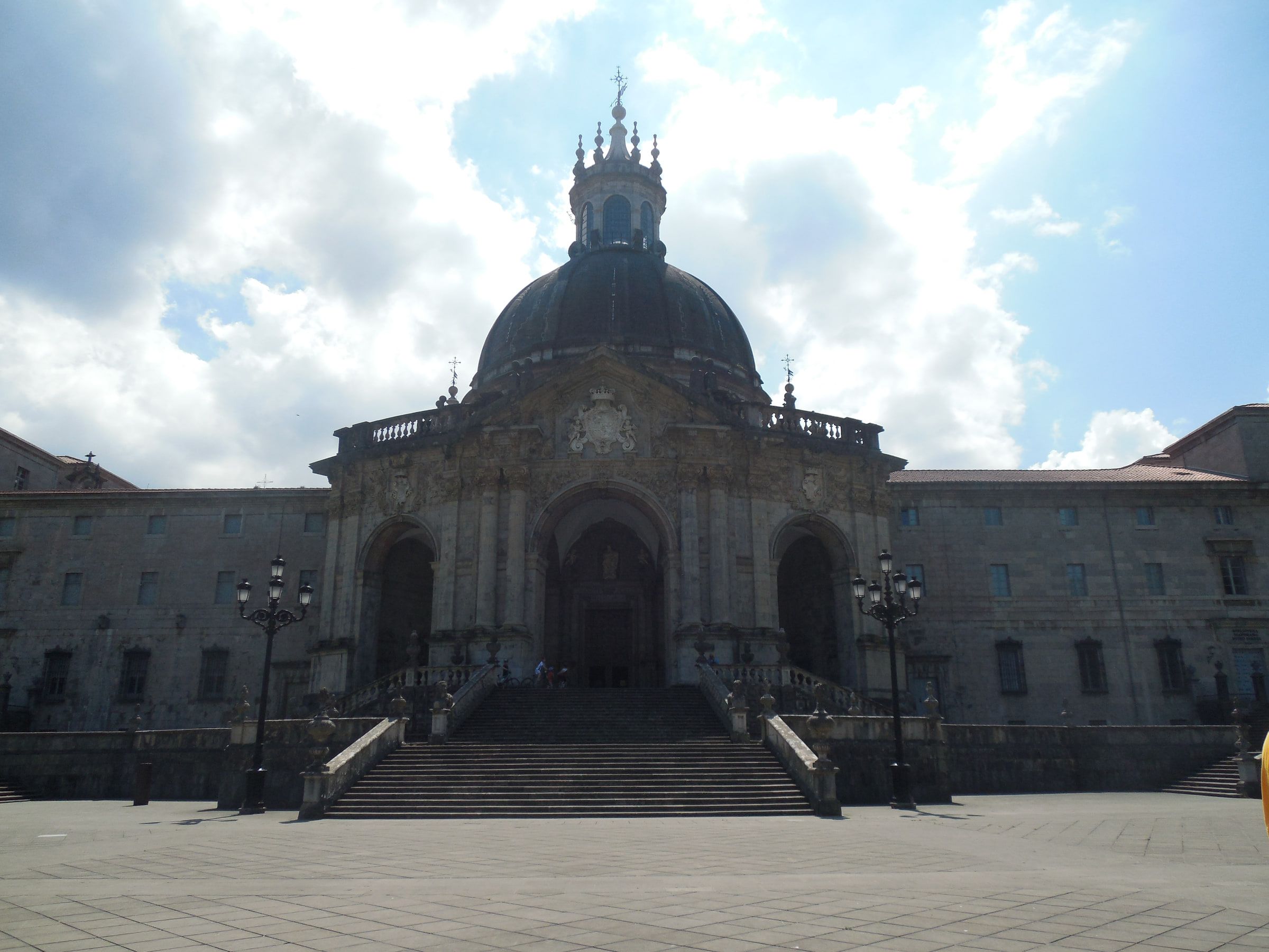 A domed baroque sanctuary of grey stone with a broad flight of steps rising to its doors