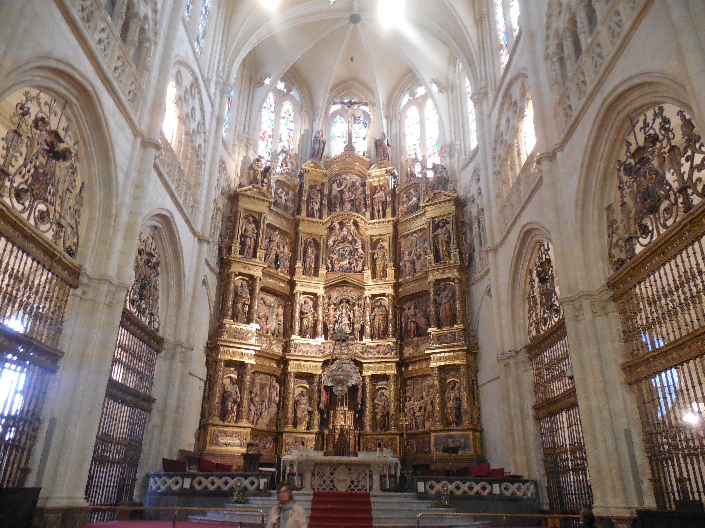 The interior of a Gothic cathedral looking toward a tall gilded altarpiece between stone piers
