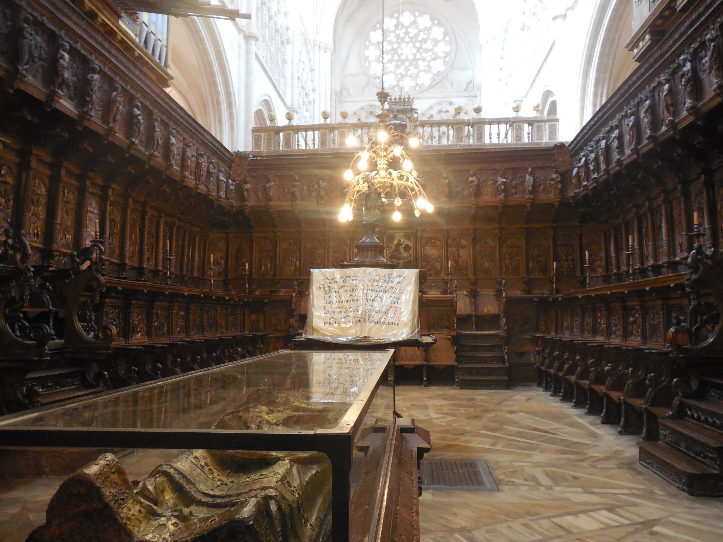 Carved wooden choir stalls in two tiers around a hanging chandelier, a stone tomb effigy in the foreground
