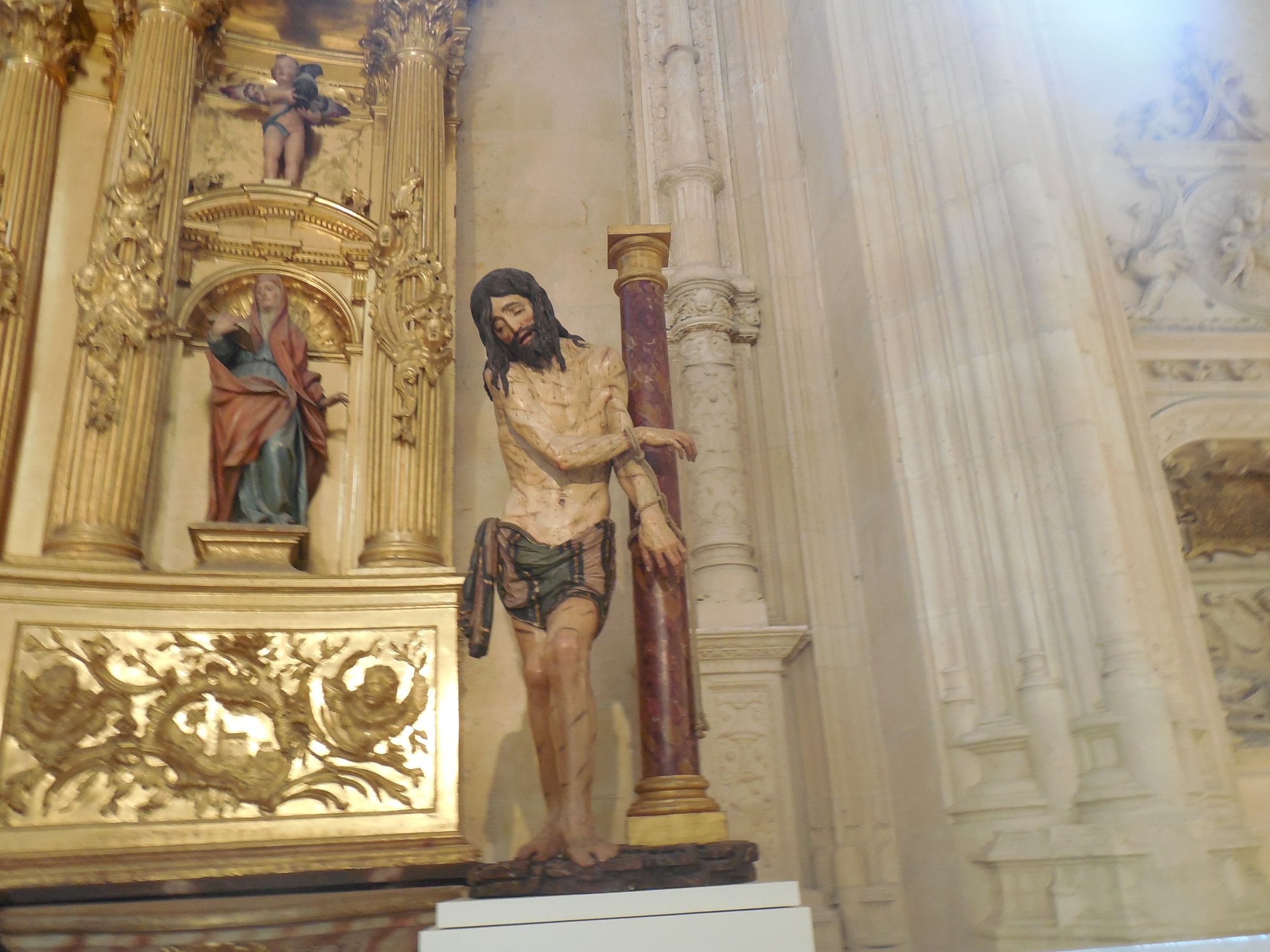 A gilded altarpiece framing a painted figure bound to a column, carved gold on every side