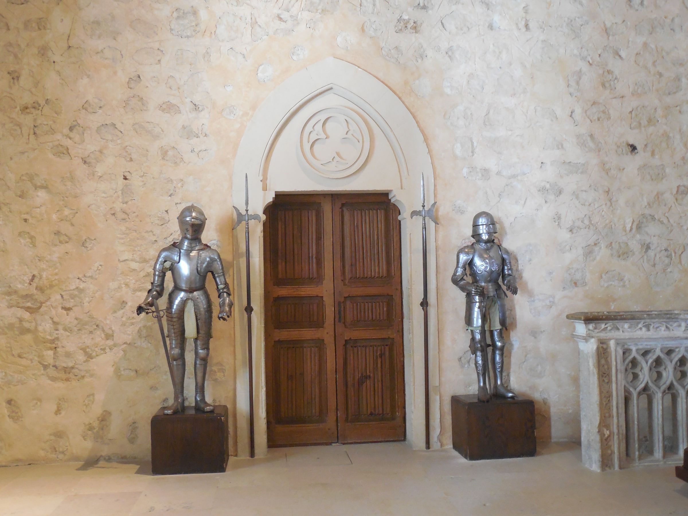 Two suits of plate armour standing either side of a wooden door in a plain stone hall