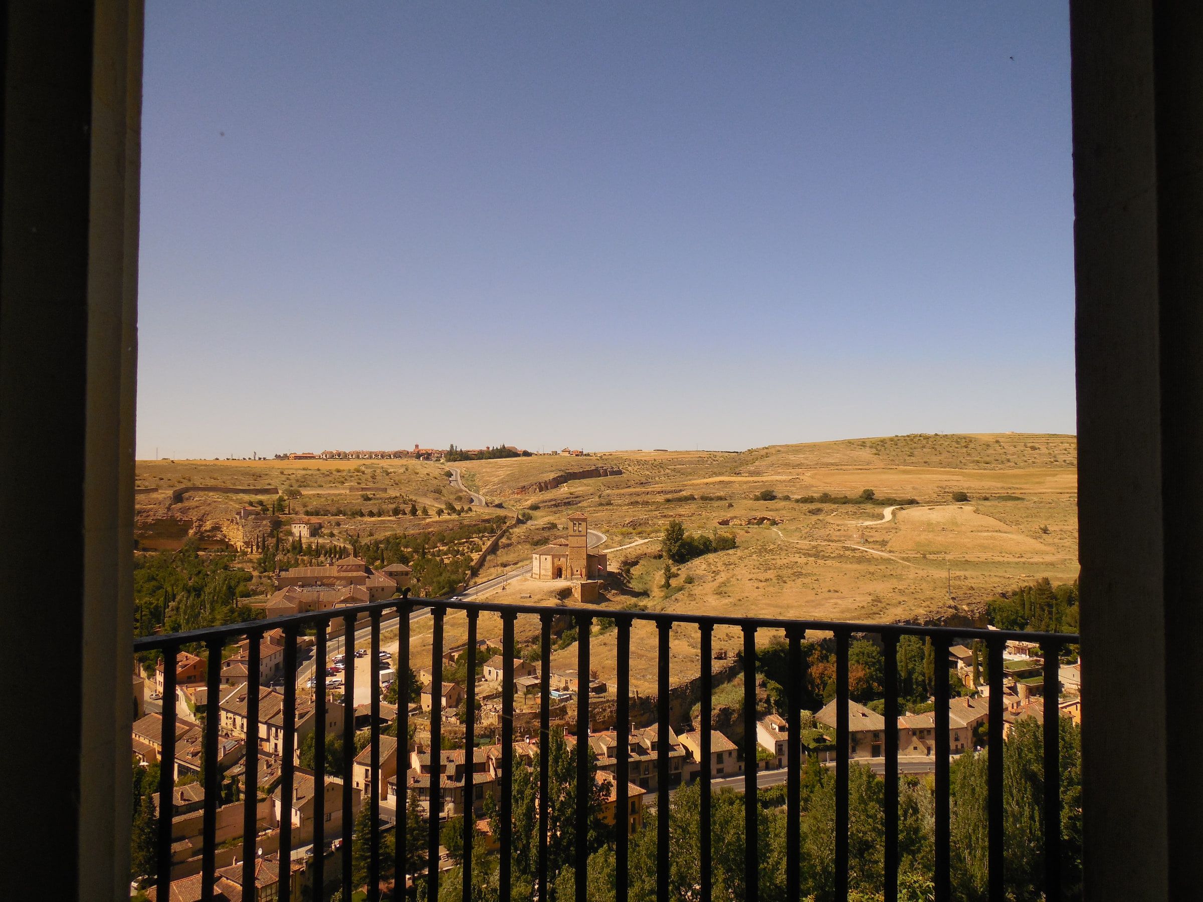 A view over dry rolling countryside from a castle balcony, seen through iron railings