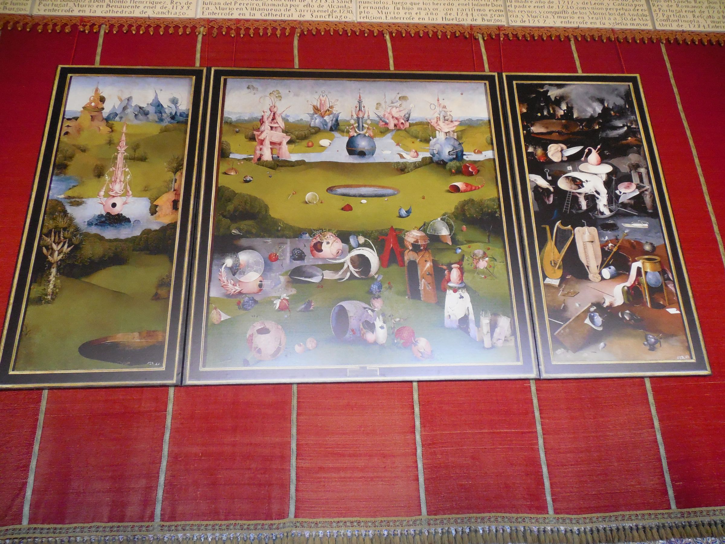 A large three-panel painting of crowded fantastical figures and landscapes, hung against a red wall