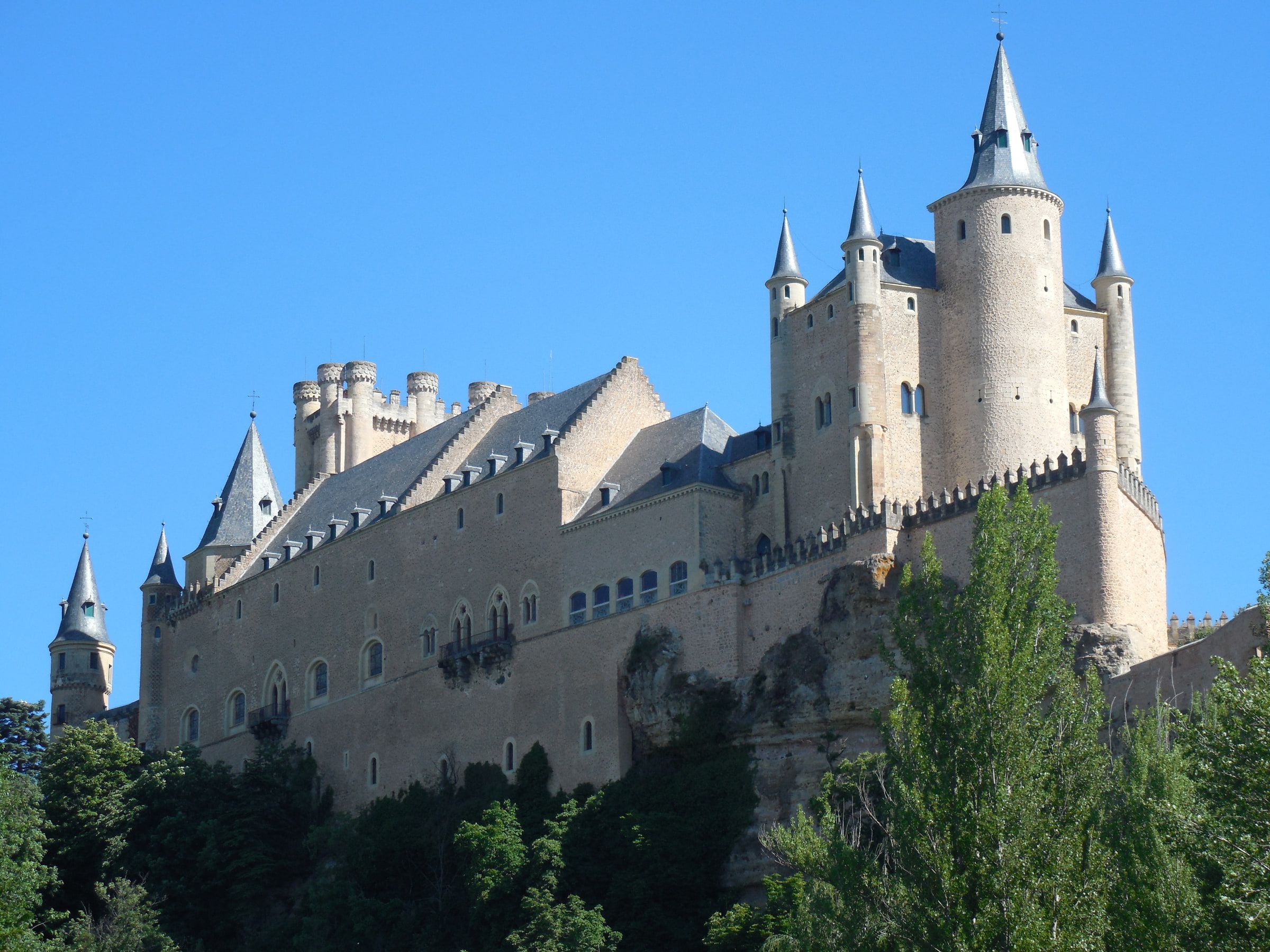 A castle on a rock outcrop seen from below, turrets and a prow-like end rising above trees