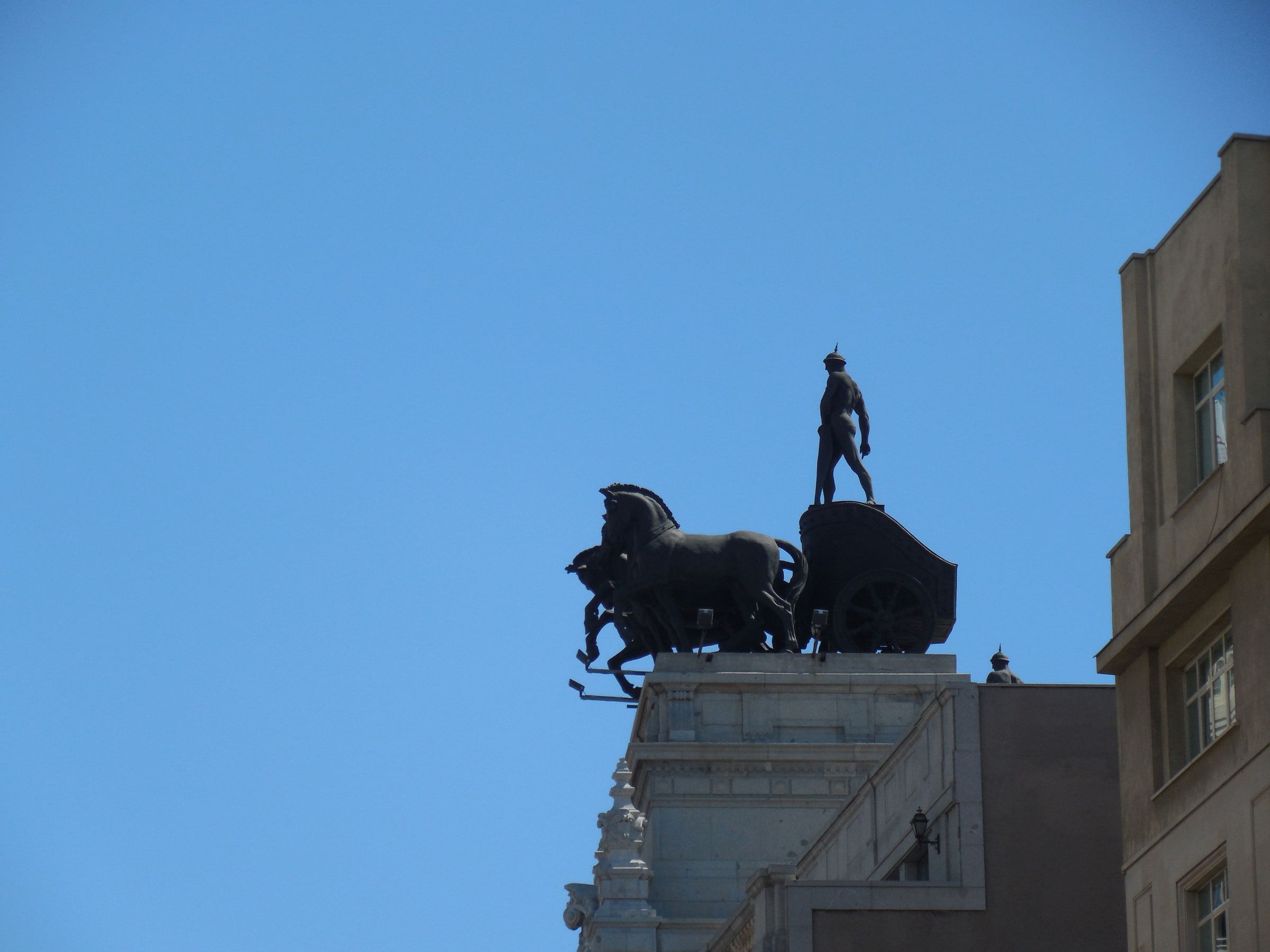 A bronze four-horse chariot statue standing on a rooftop against a clear blue sky