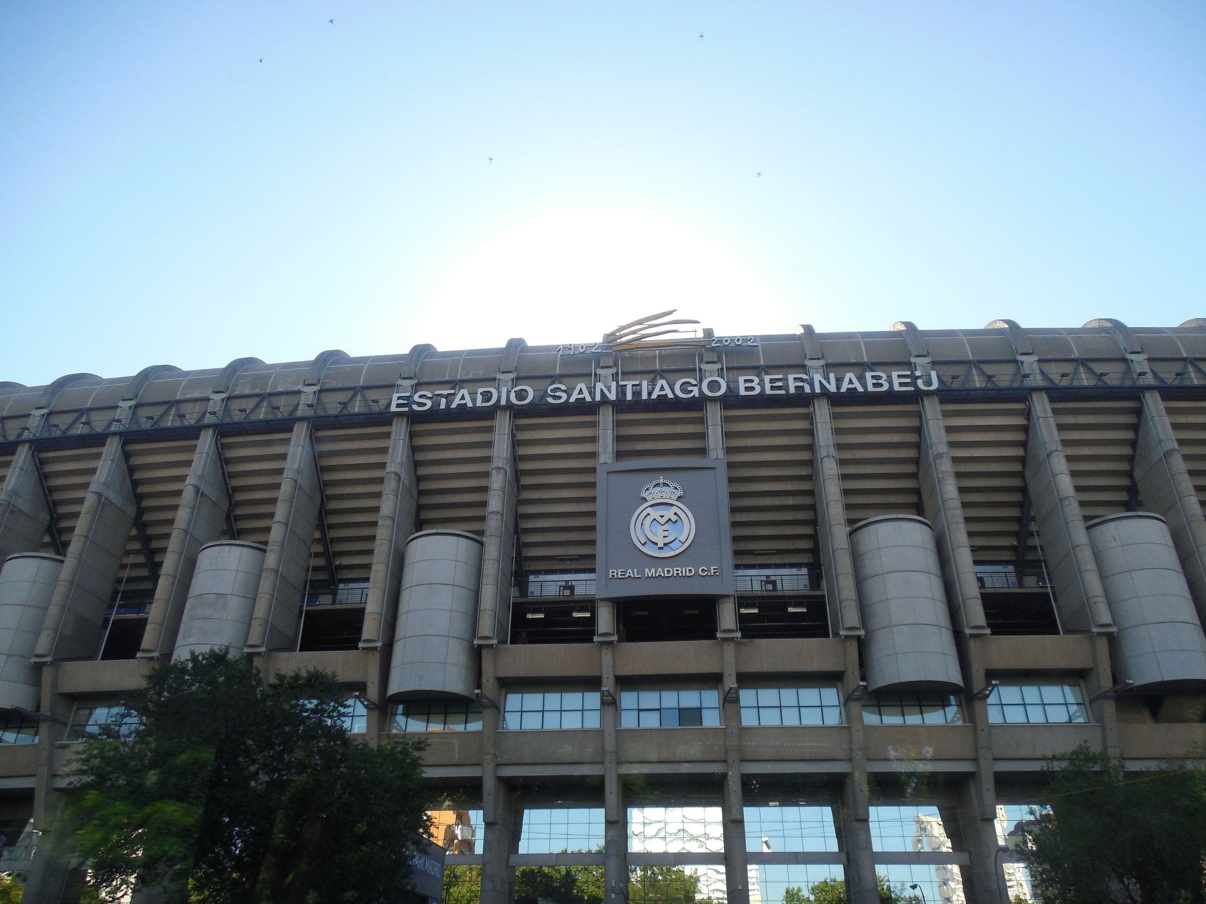 The exterior of a large football stadium, its name and club crest mounted across the concrete