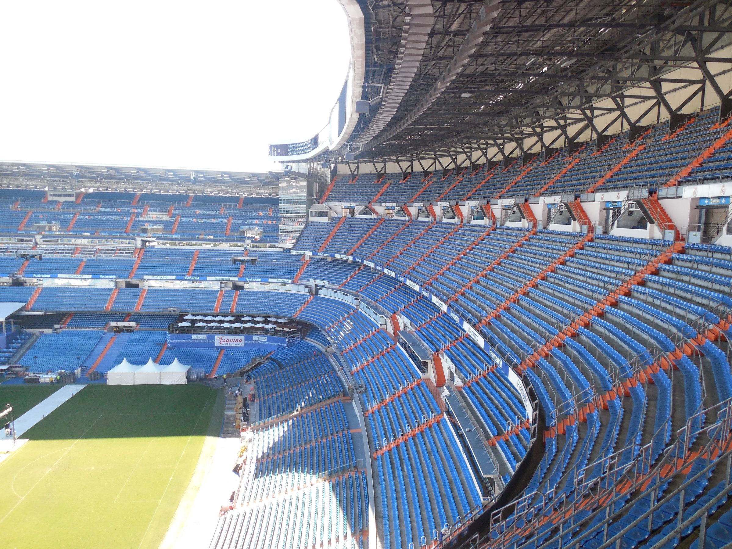 Steep tiers of blue and orange seating curving around an empty stadium bowl