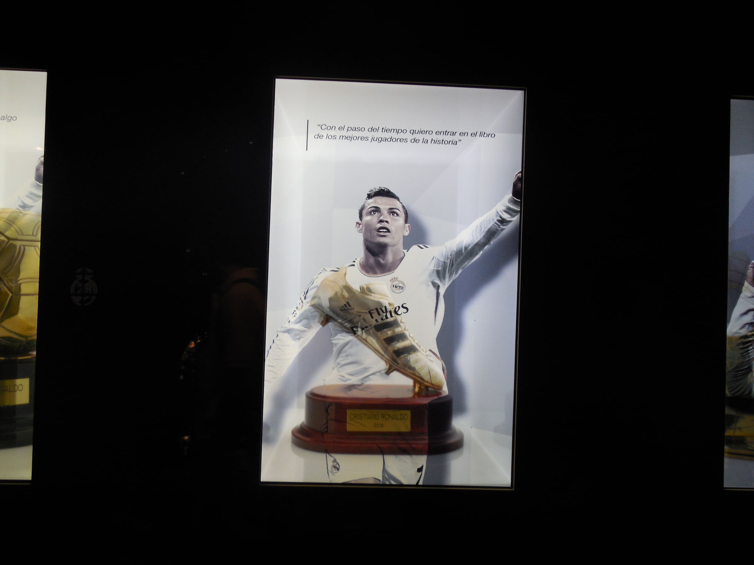 A lit display case holding a golden boot trophy beneath a large photograph of a footballer celebrating