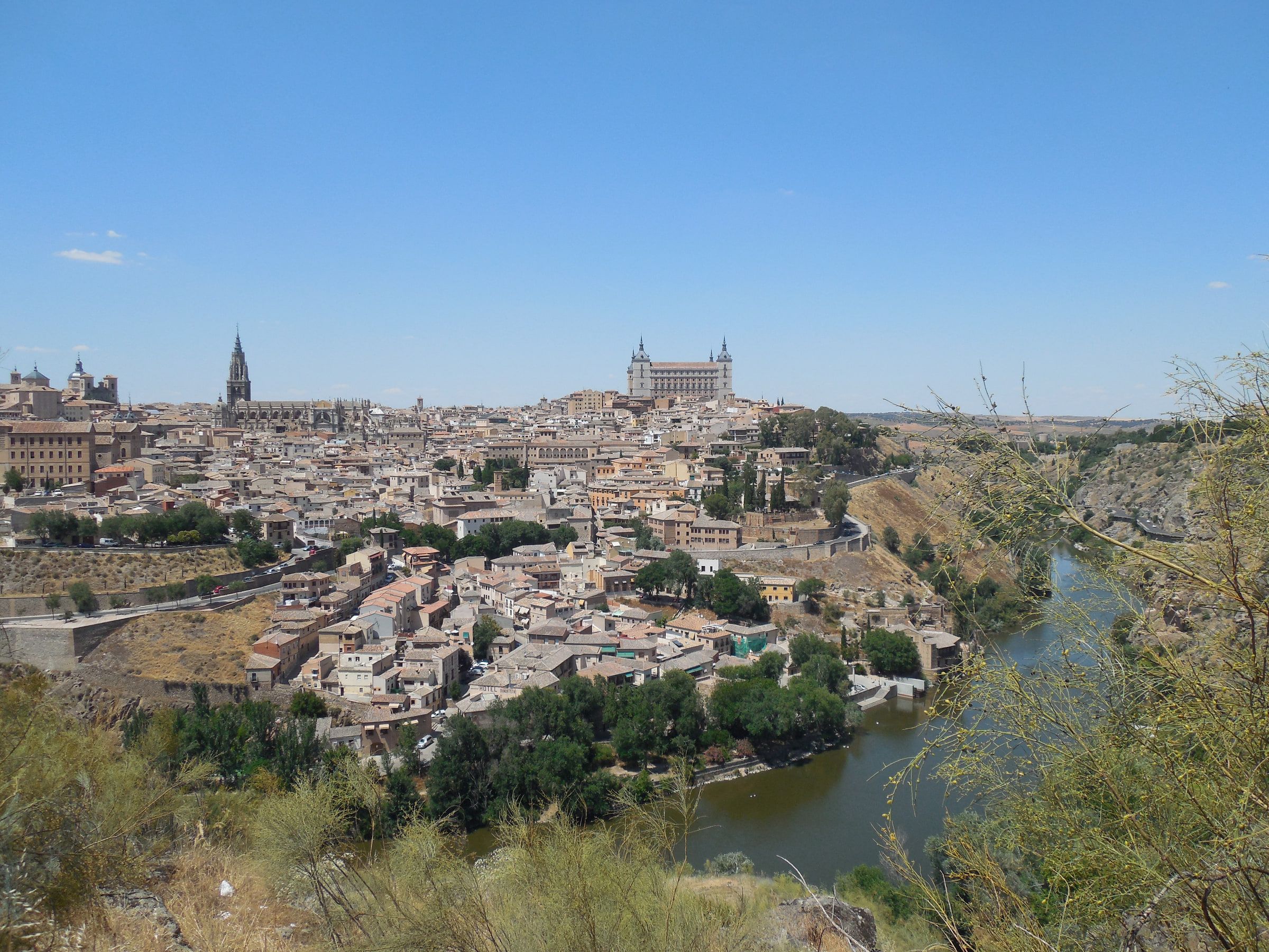 A hillside city of pale stone above a river gorge, a large square fortress standing on the skyline