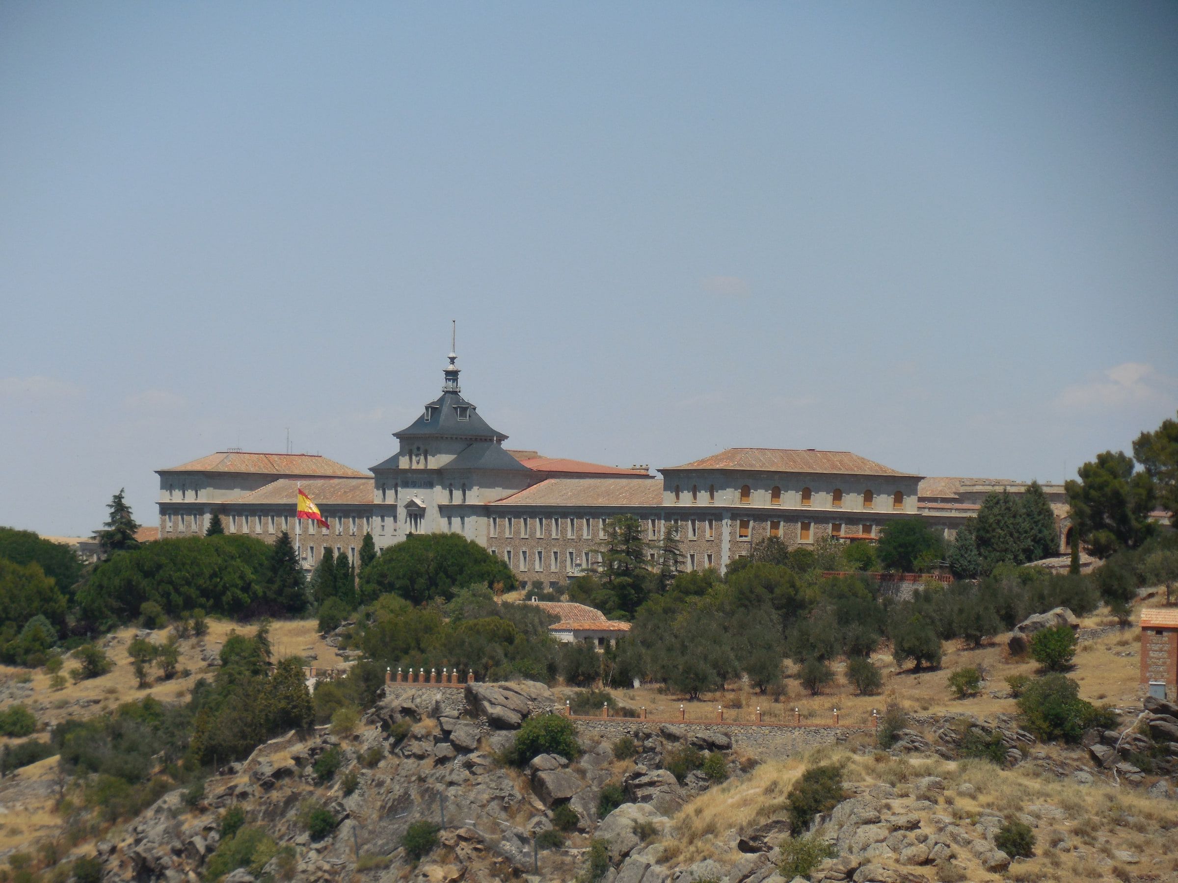 A large symmetrical institutional building on a ridge above scrub, a flag at its centre
