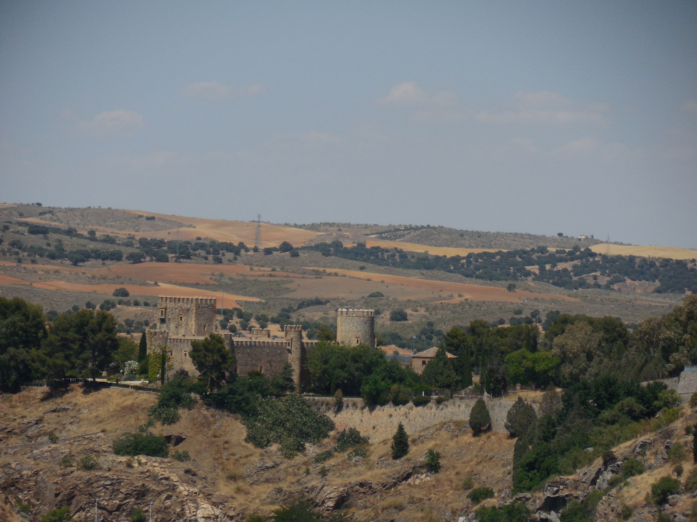 A small castle with square towers and curtain walls standing in dry open countryside